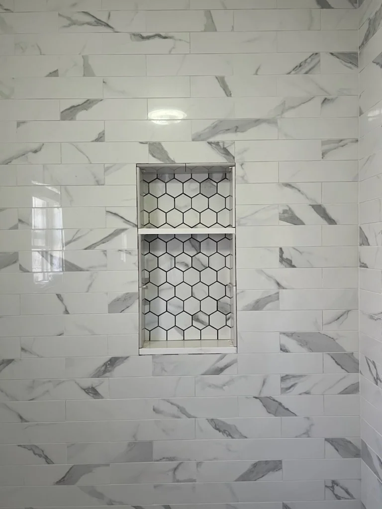 White marble subway tile shower with staggered pattern and hexagonal tile niche accent