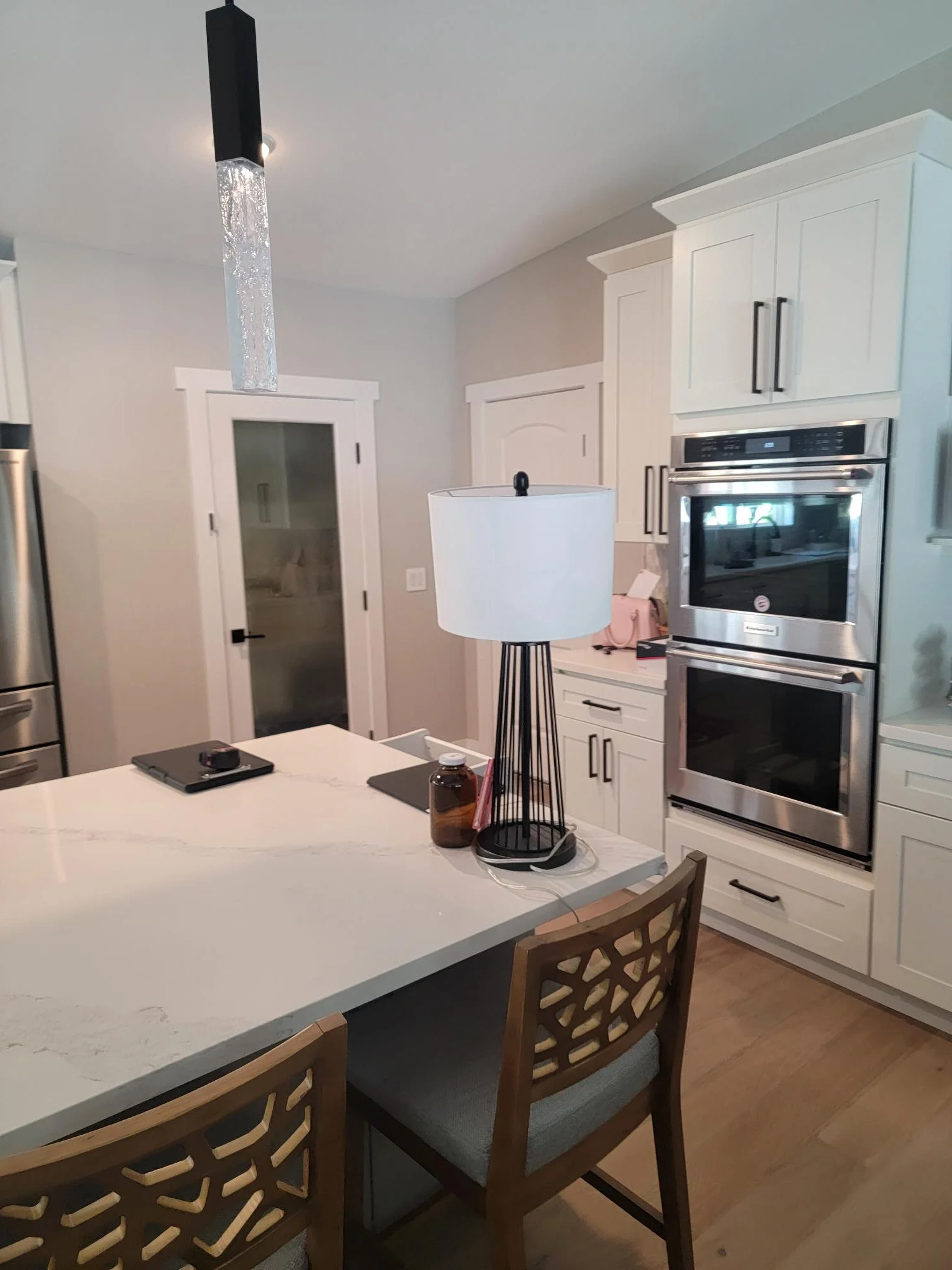 White kitchen cabinetry with quartz island, stainless steel double ovens, and modern pendant lighting
