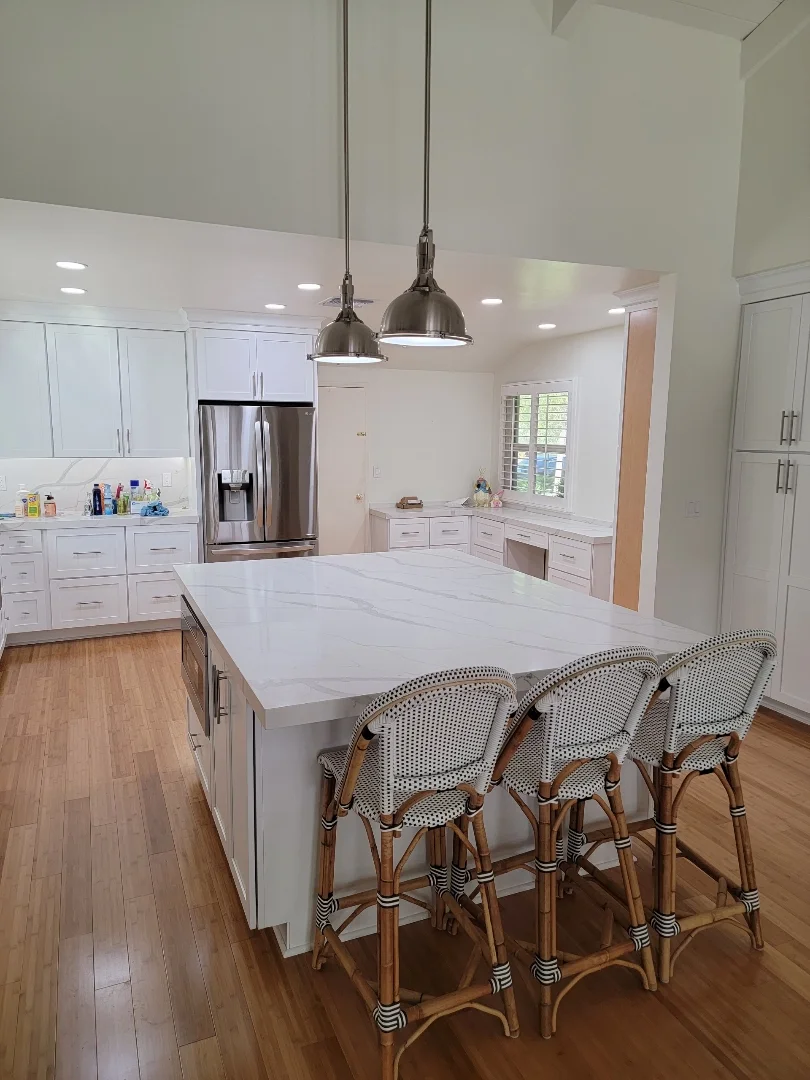 White kitchen with quartz island, stainless steel appliances, pendant lights, and hardwood flooring