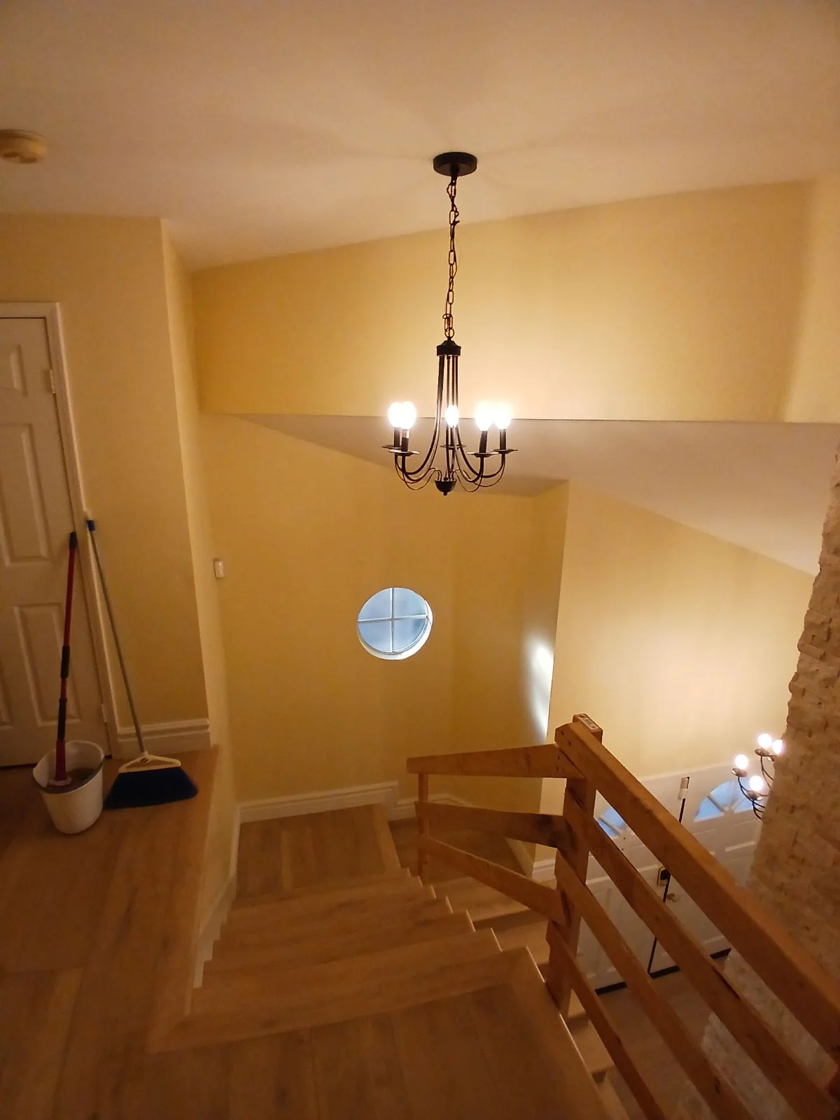 Stairwell with yellow walls, black chandelier, wooden railings, and circular window