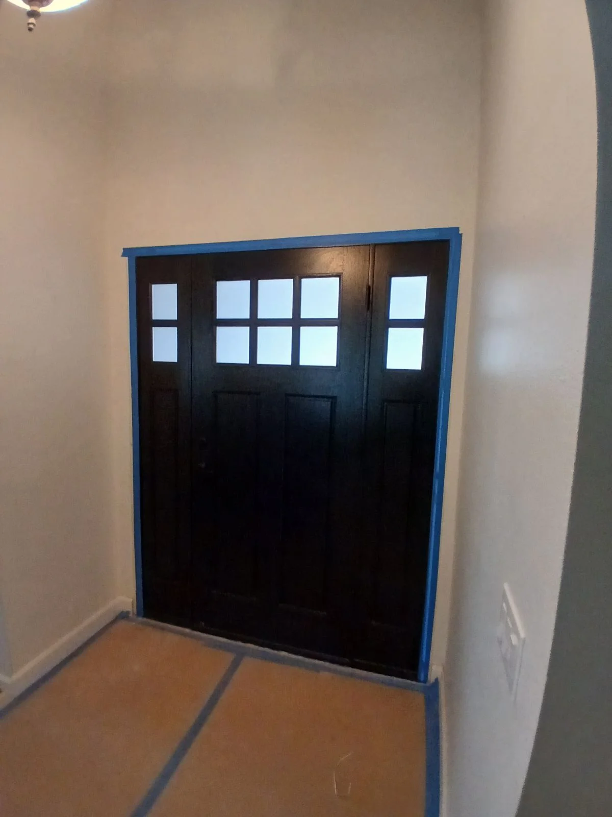 Black garage door with glass panels and blue trim frame installed in white drywall opening