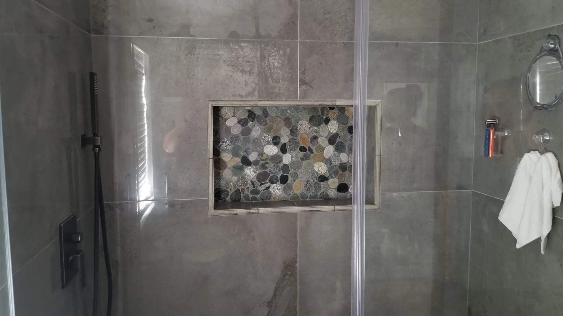 Gray tile shower with pebble mosaic accent niche, frameless glass enclosure, and chrome fixtures