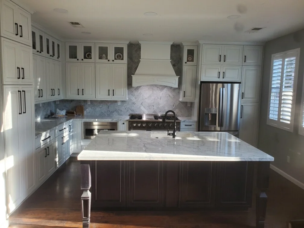 White kitchen cabinetry with marble countertops, island, and stainless steel appliances