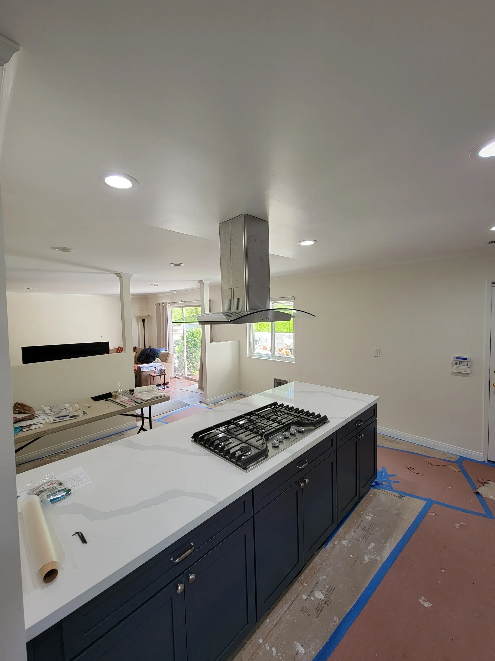 Kitchen island with white quartz counters, black cabinets, gas range, and stainless steel hood during construction