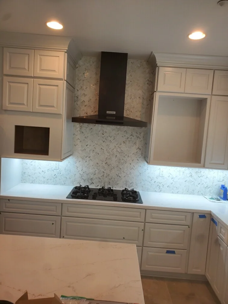 Kitchen with cream cabinetry, marble backsplash, white quartz counters, and black range hood
