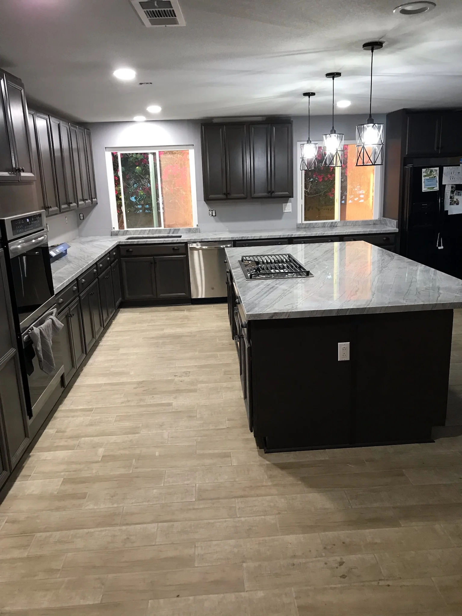 Modern kitchen with dark cabinets, marble countertops, stainless steel appliances, and wood-look flooring