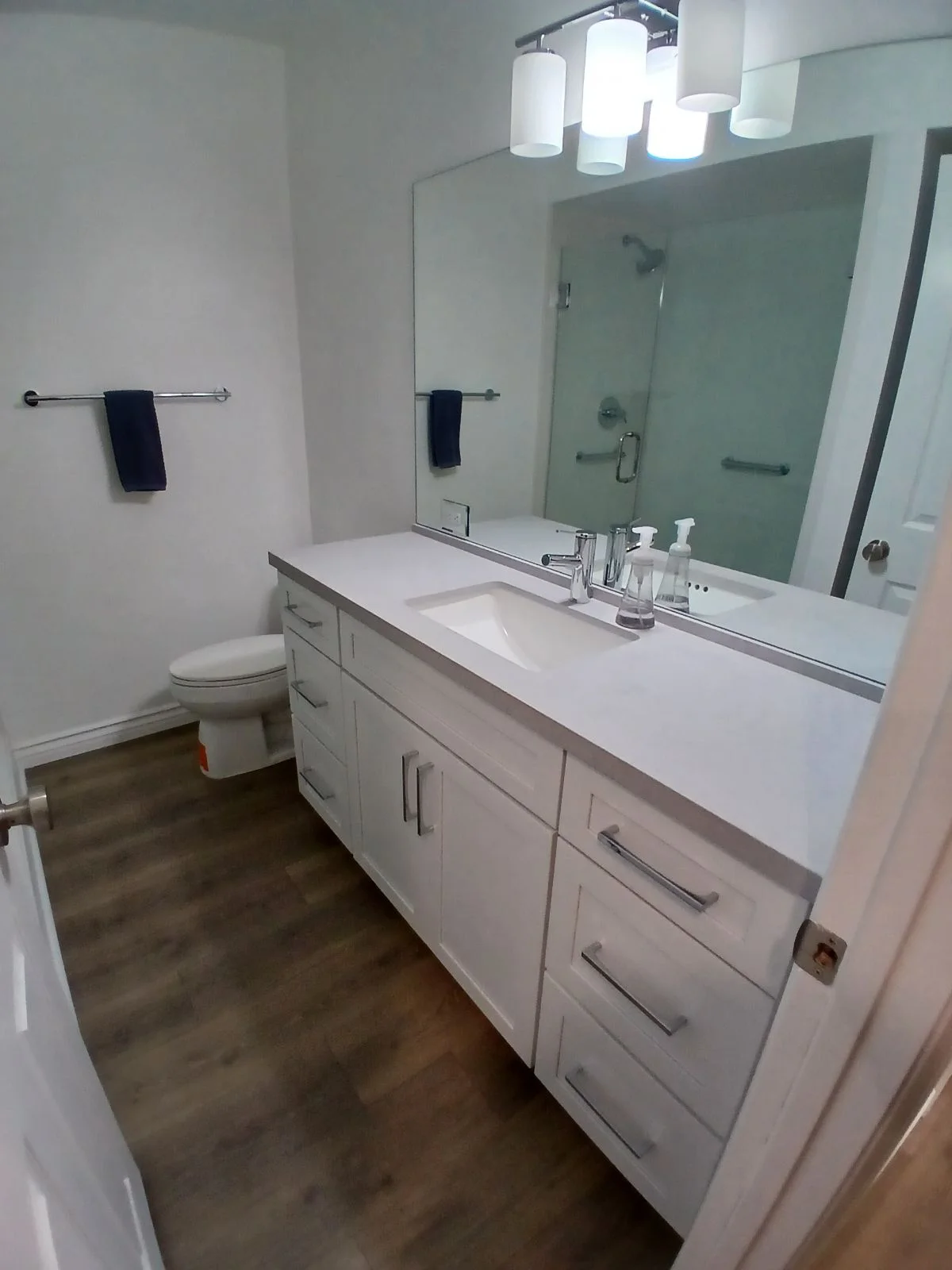 White vanity with quartz countertop, frameless glass shower, and vinyl plank flooring