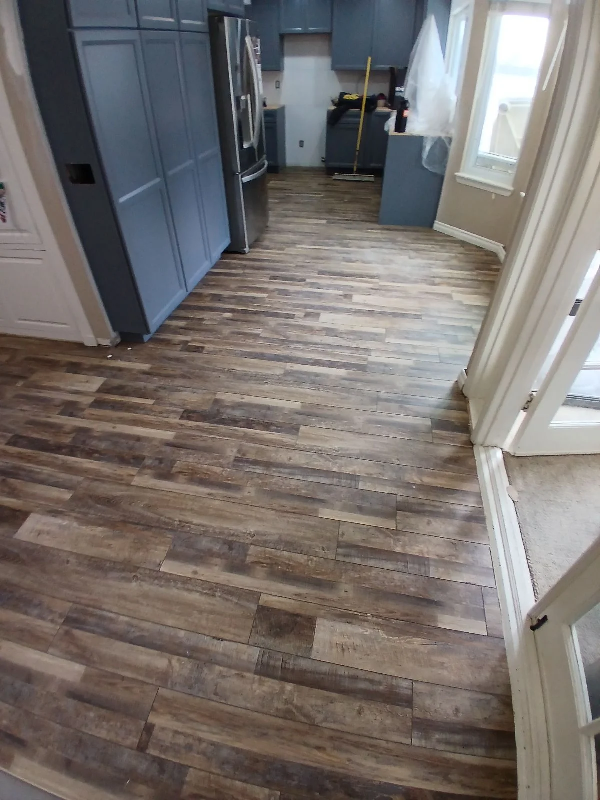 Engineered wood plank flooring installed in kitchen with blue cabinetry and stainless steel appliances