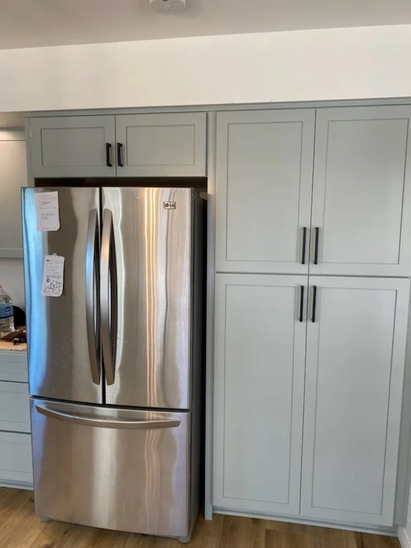 Light gray kitchen cabinets with recessed panels and stainless steel refrigerator installation