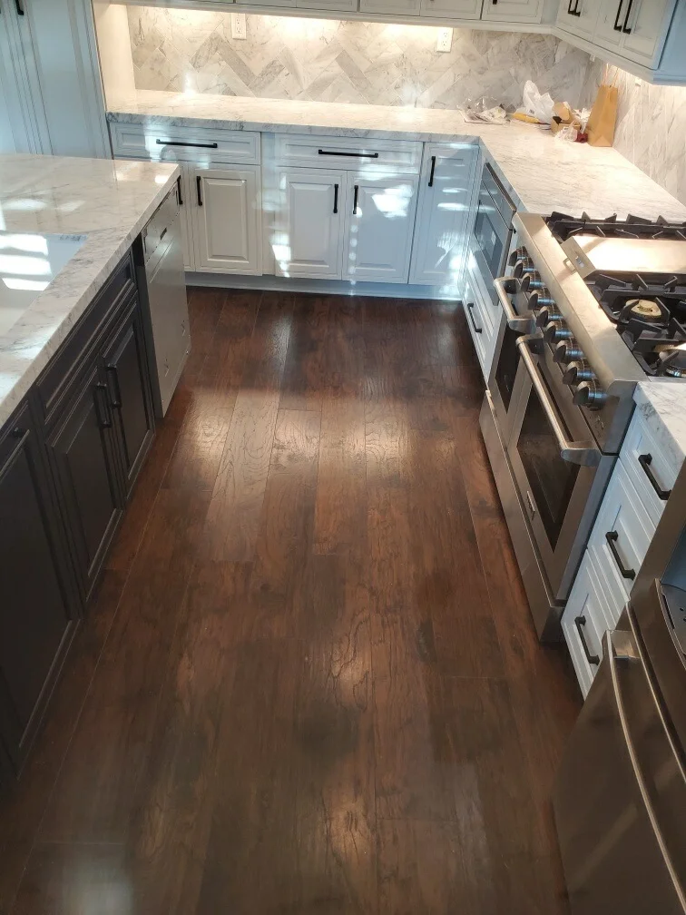 Kitchen with white cabinetry, marble counters, herringbone backsplash, and dark hardwood floors