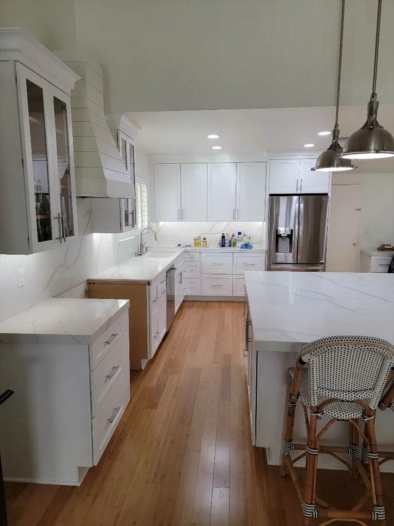 White kitchen with shaker cabinets, quartz counters, stainless steel appliances, and hardwood flooring