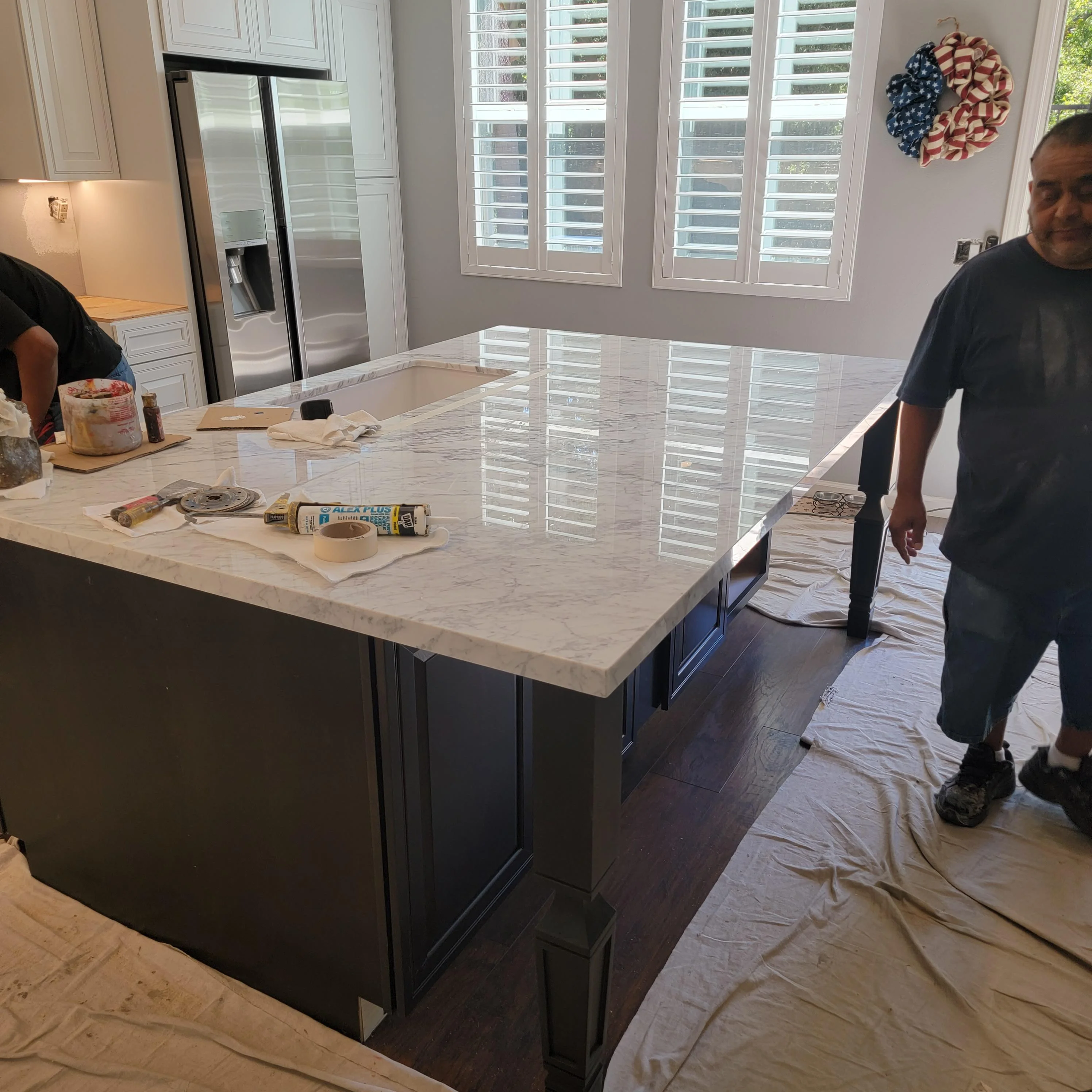 Marble countertop kitchen island with dark base cabinetry and black hardware during installation