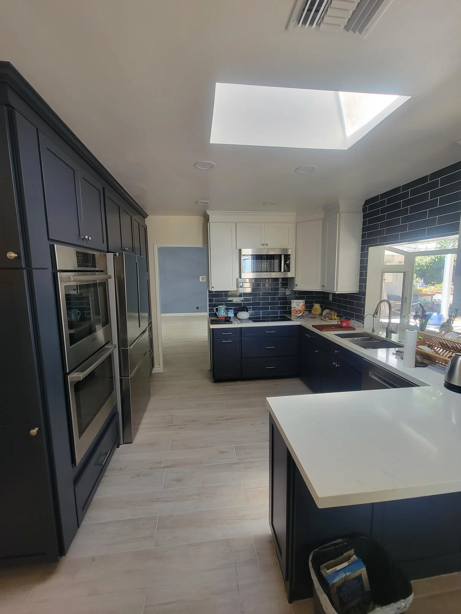 Modern kitchen with dark navy and white cabinets, subway tile backsplash, white quartz counters, and skylight