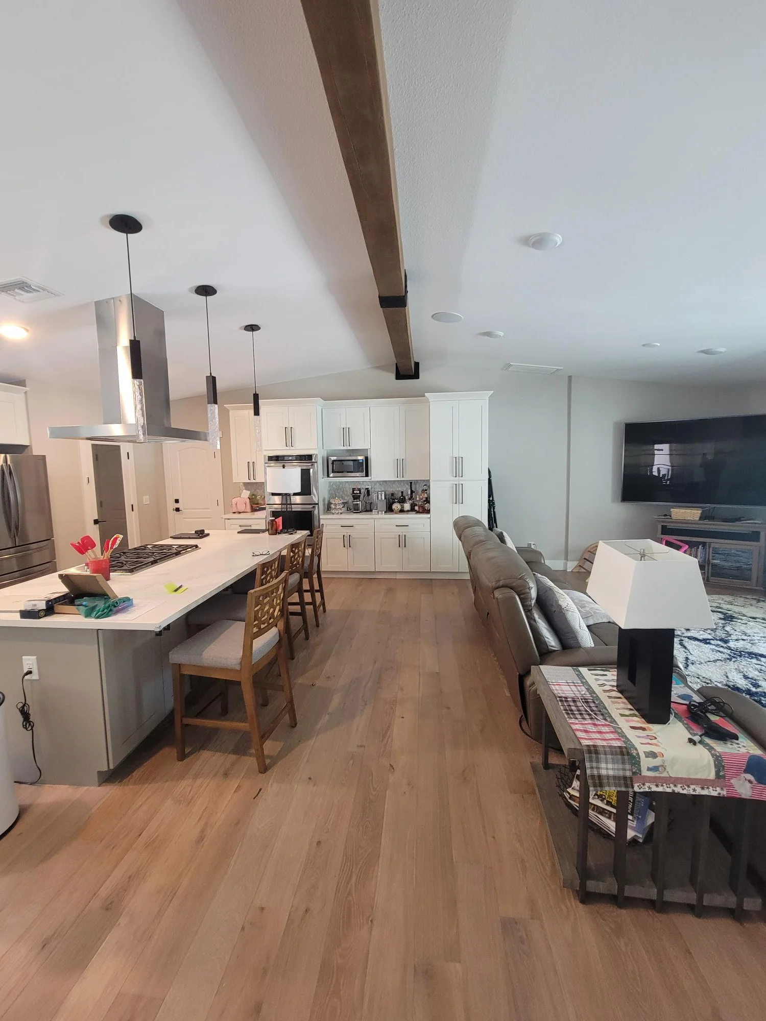 Modern kitchen with white cabinets, stainless steel appliances, quartz island, hardwood floors, and exposed beam ceiling