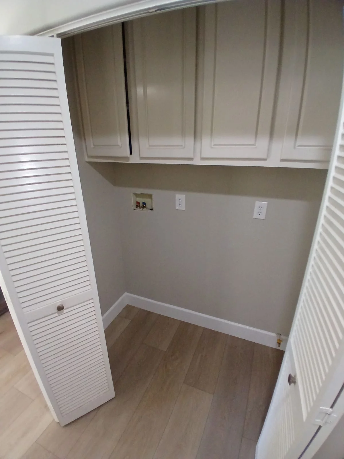 White shaker cabinetry, louvered doors, and electrical outlets in laundry room with wood flooring