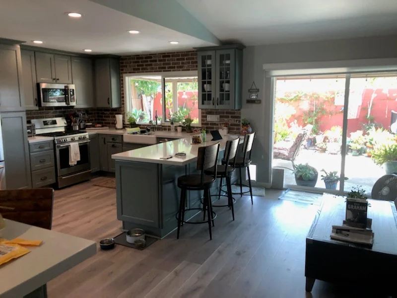 Kitchen with gray cabinetry, stainless steel appliances, brick backsplash, island seating, and hardwood floors