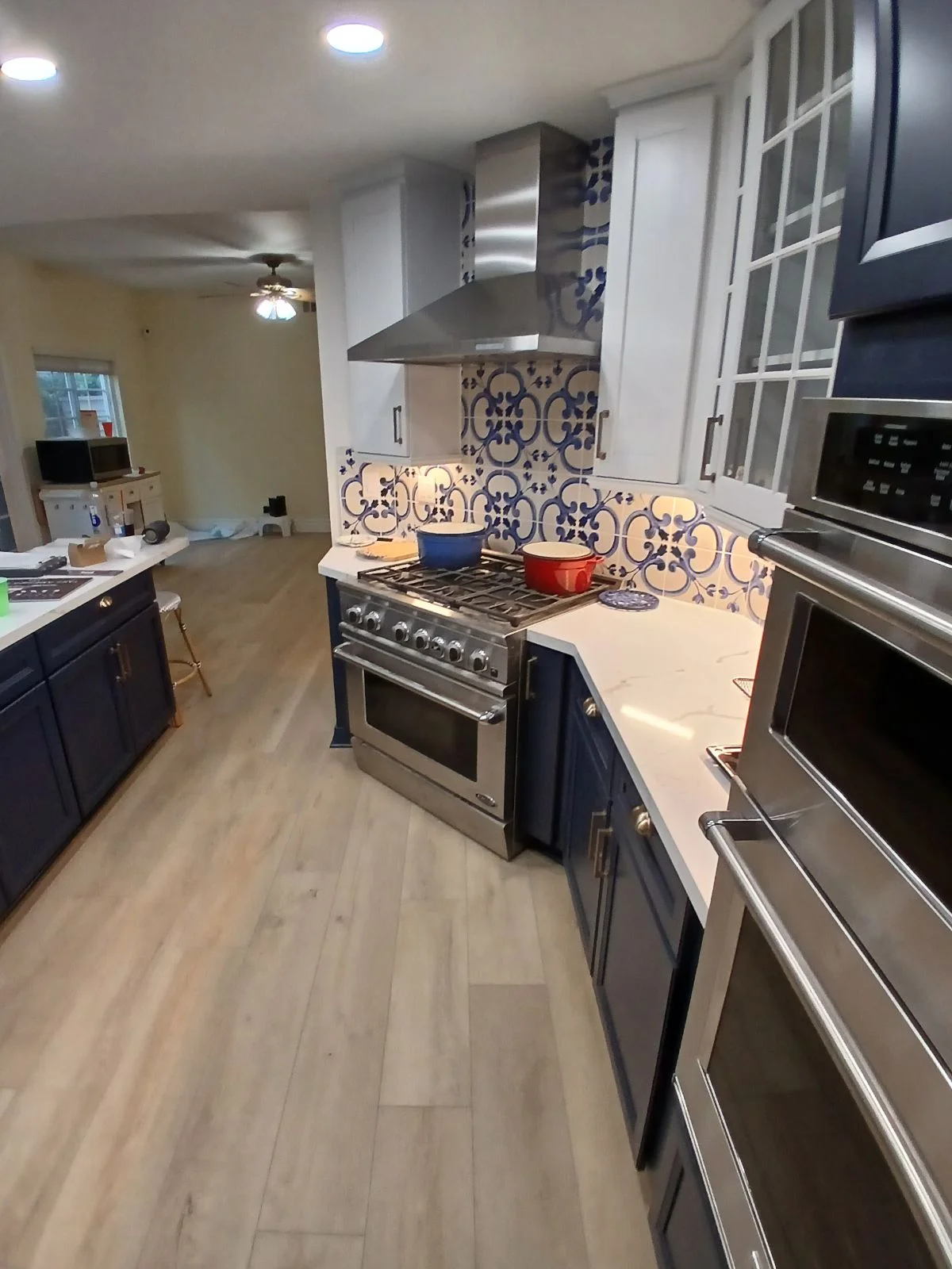 Kitchen with blue patterned tile backsplash, stainless steel hood and appliances, white cabinets, wood flooring