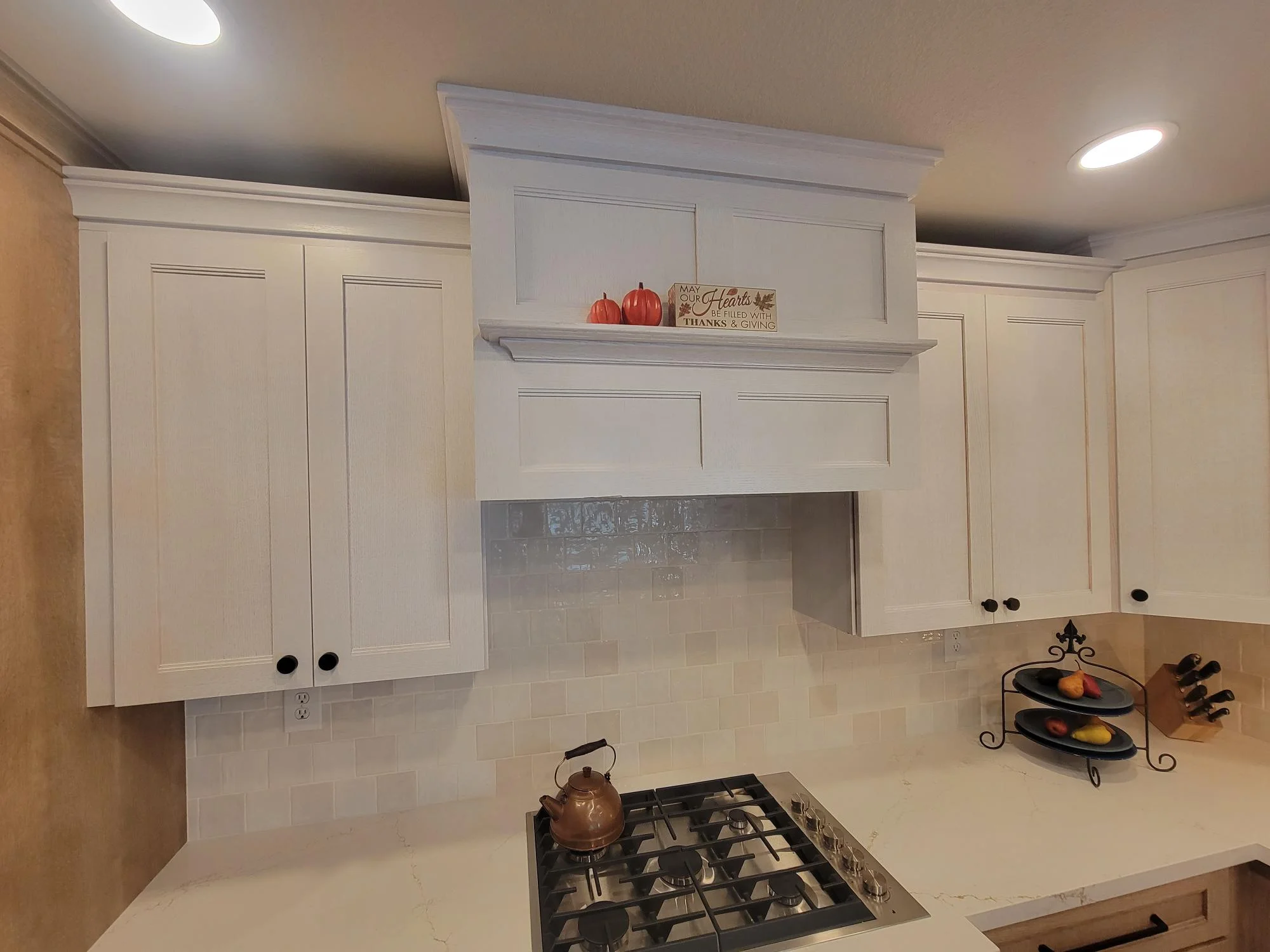 White kitchen cabinets, subway tile backsplash, gas cooktop, and fireplace surround with floating shelf