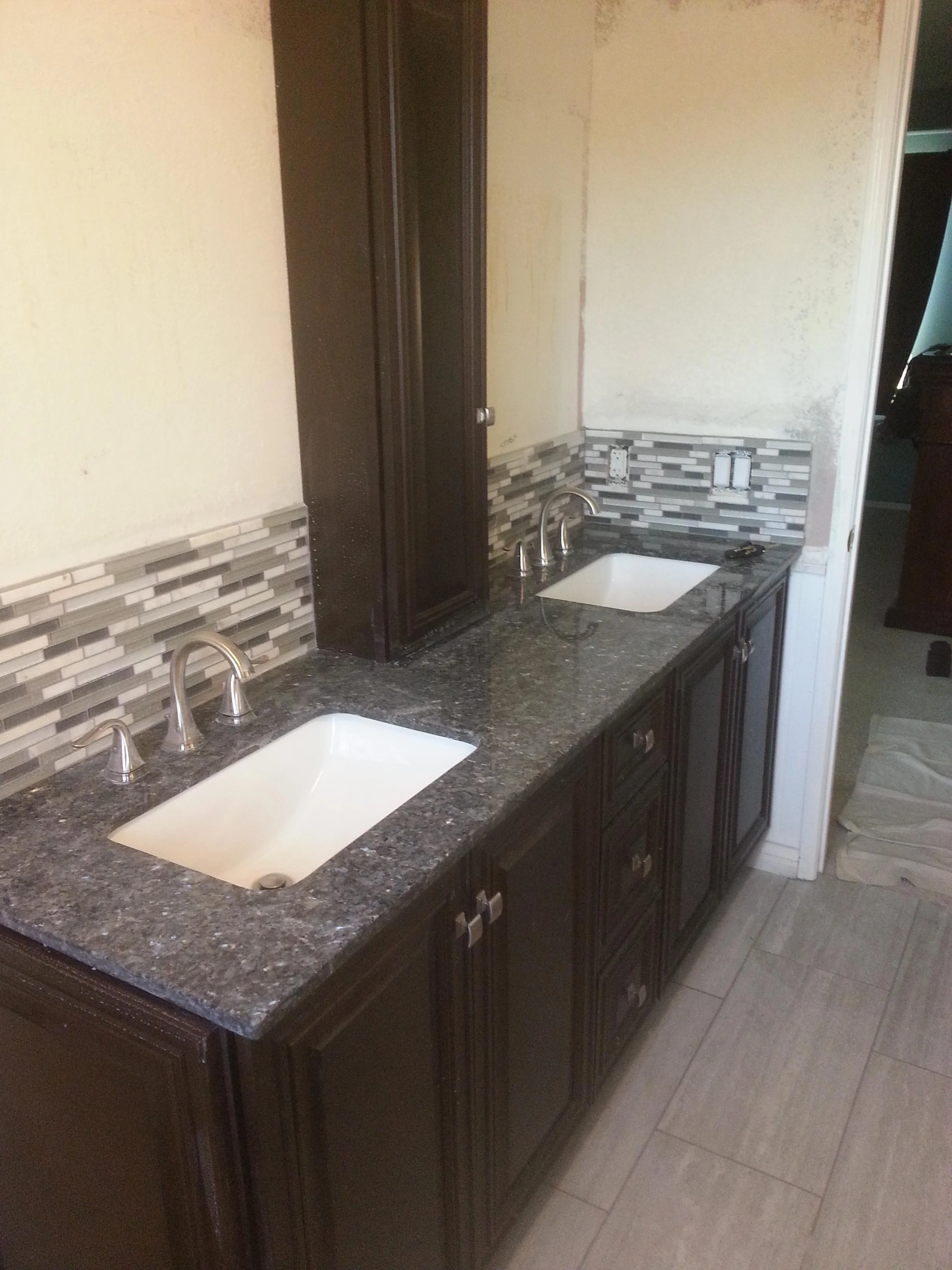 Dual-sink bathroom vanity with granite countertop and linear glass tile backsplash