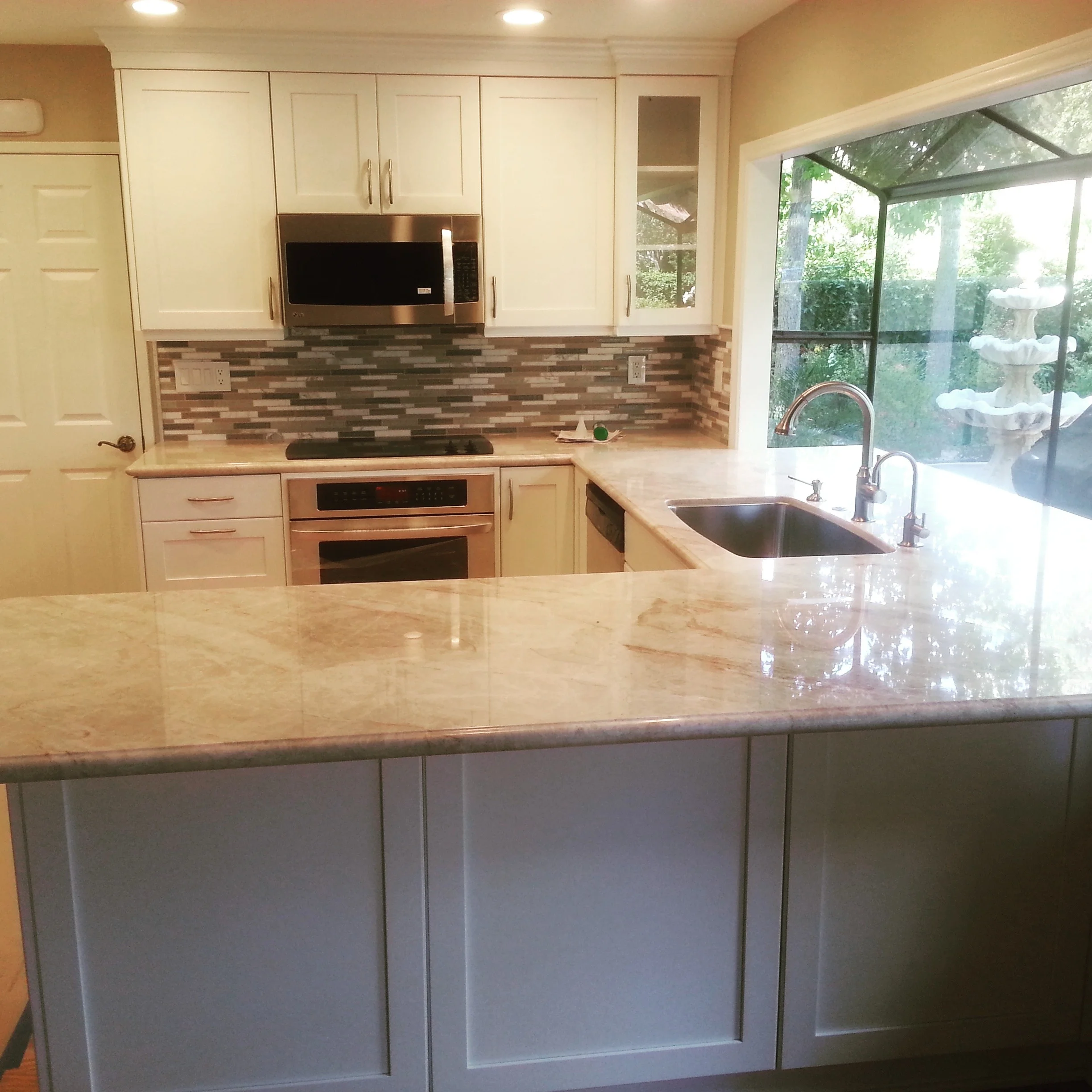 Kitchen with cream cabinets, quartz counters, brick backsplash, and stainless steel appliances