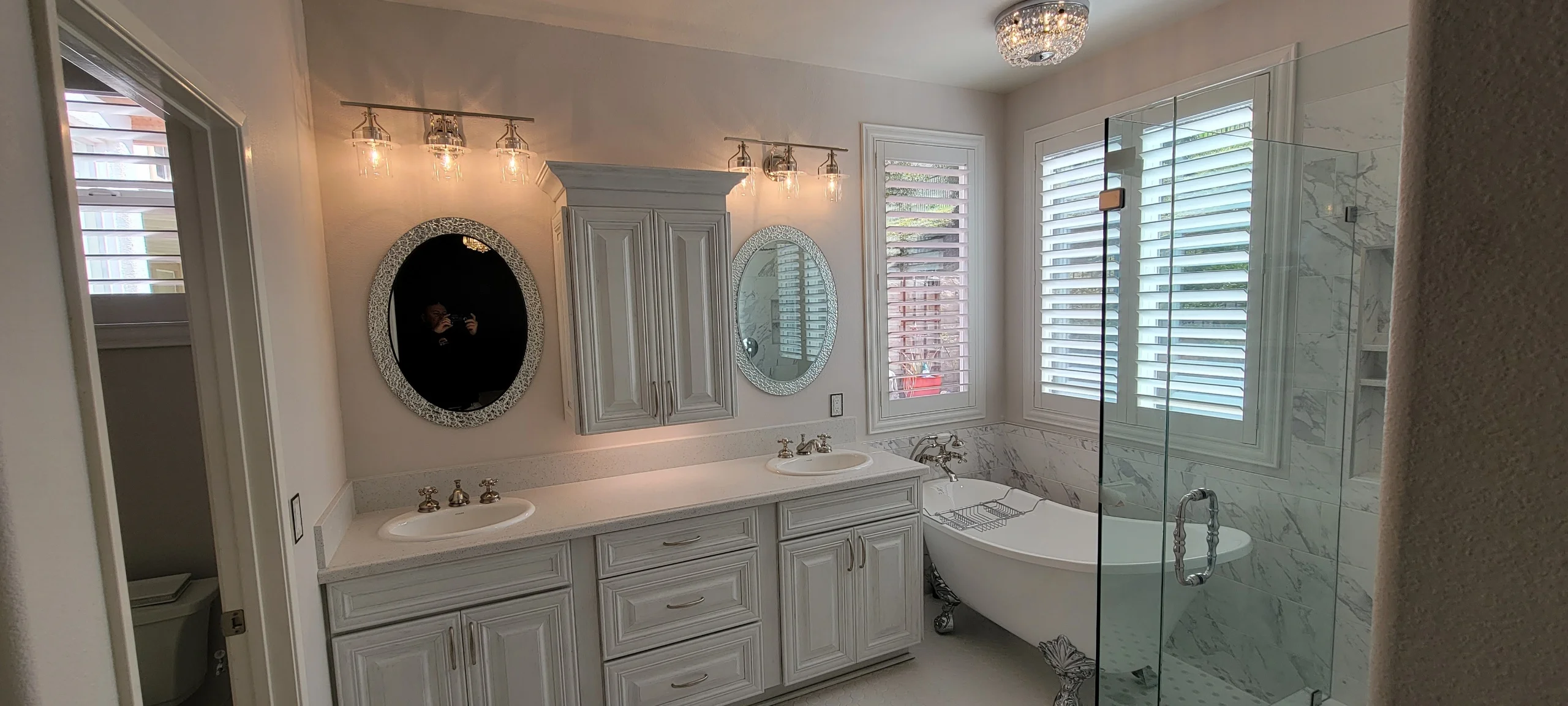 Master bathroom with white cabinetry, marble counters, dual sinks, freestanding tub, and glass shower enclosure