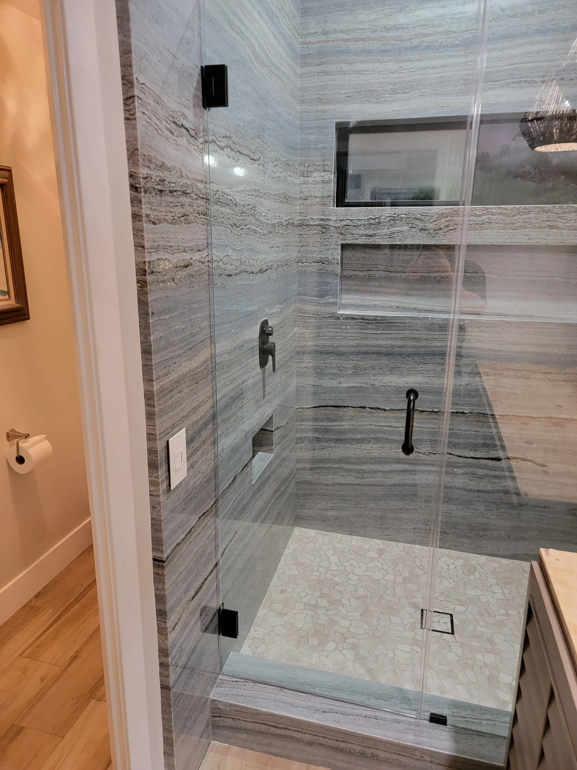 Frameless glass shower with wood-grain porcelain tile walls and marble mosaic floor