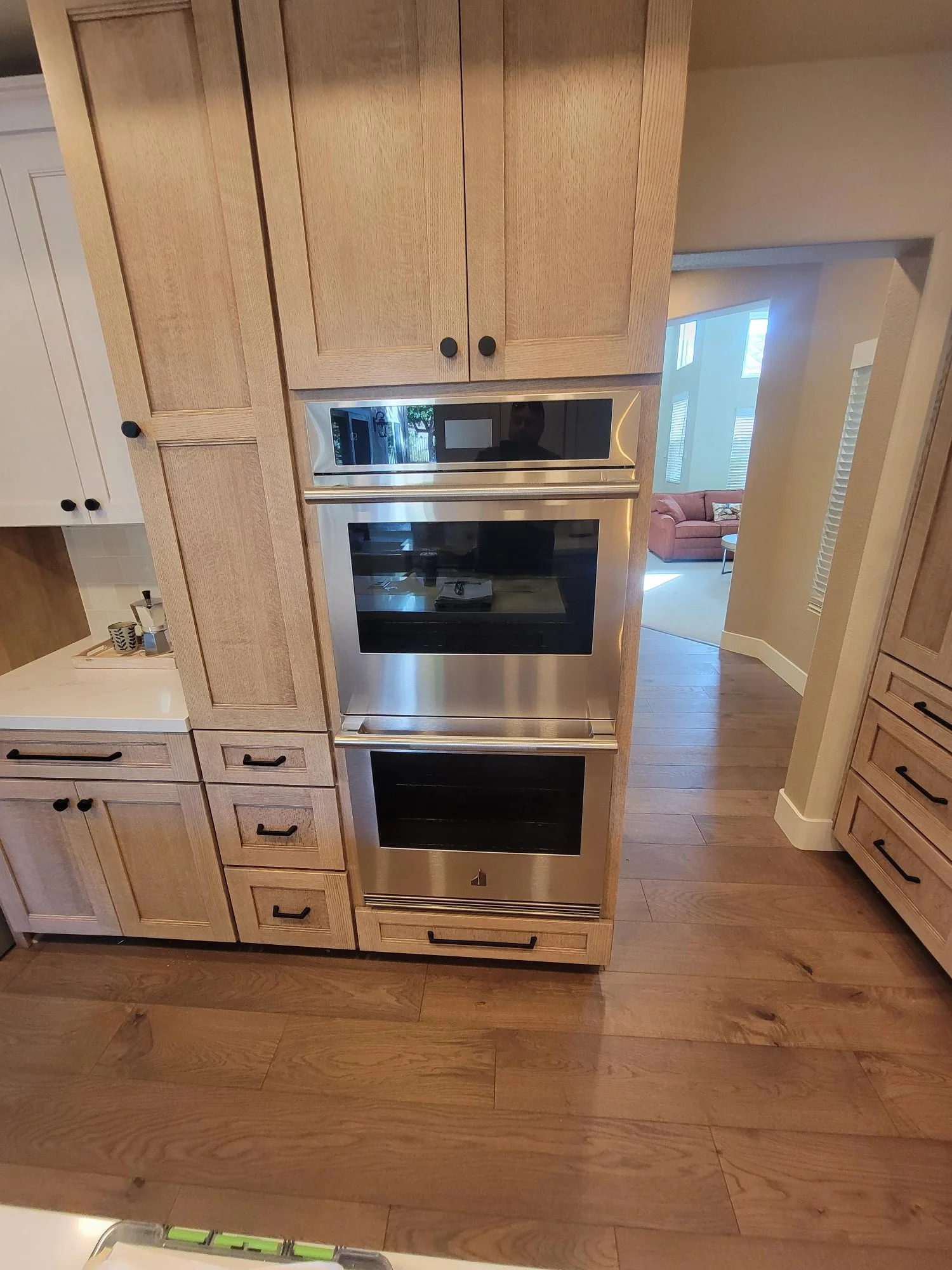 Light oak kitchen cabinetry with integrated stainless steel double wall ovens and hardwood flooring