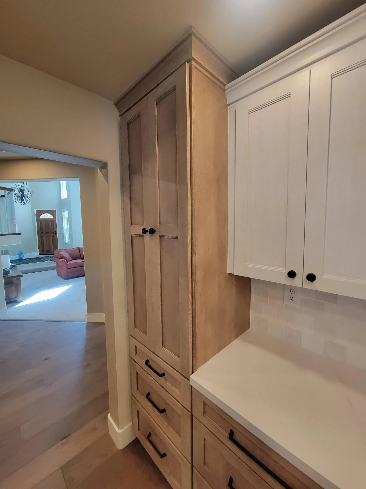 Tall wooden pantry cabinet with white painted upper cabinets and black hardware in kitchen space