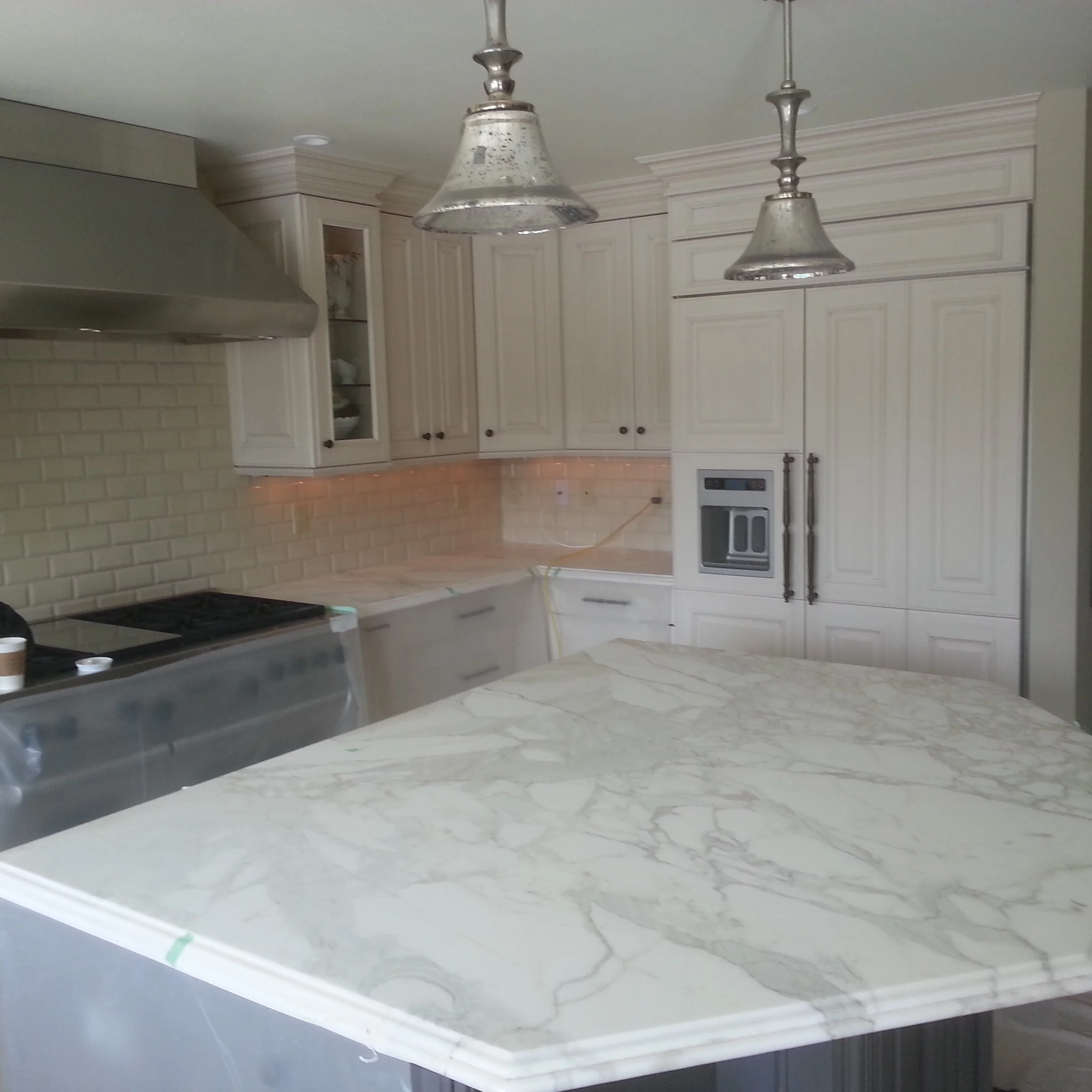 White kitchen cabinetry with marble waterfall island, subway tile backsplash, and pendant lights