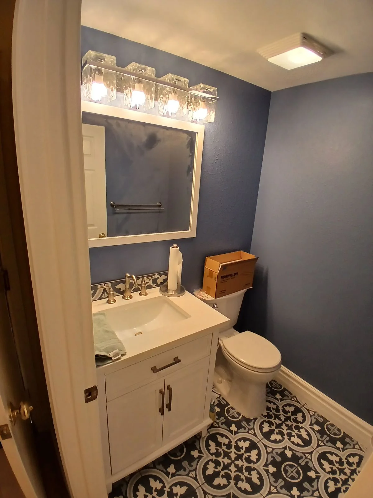 Bathroom with white vanity, slate blue walls, four-light fixture, and patterned tile floor