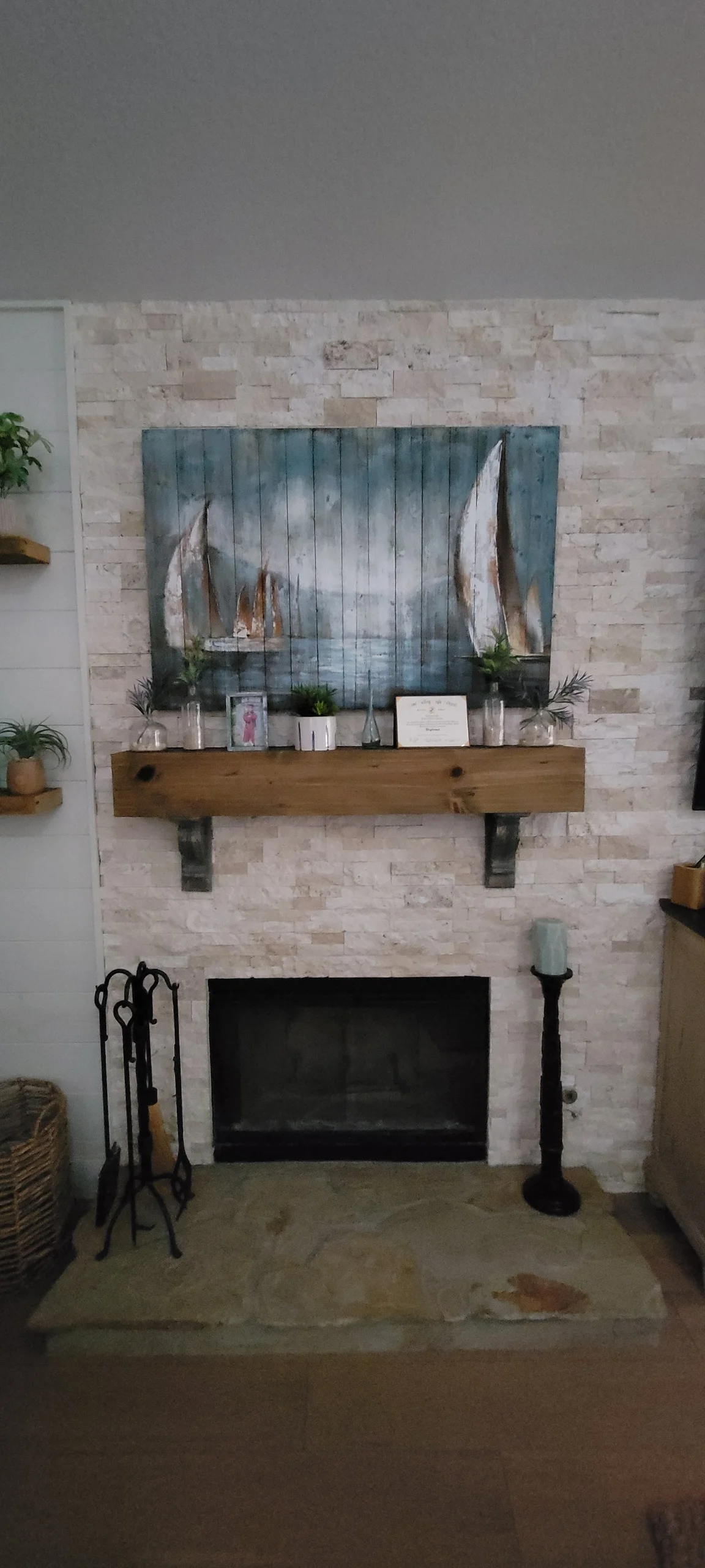 Light brick fireplace surround with wood mantel and sailboat artwork above black insert