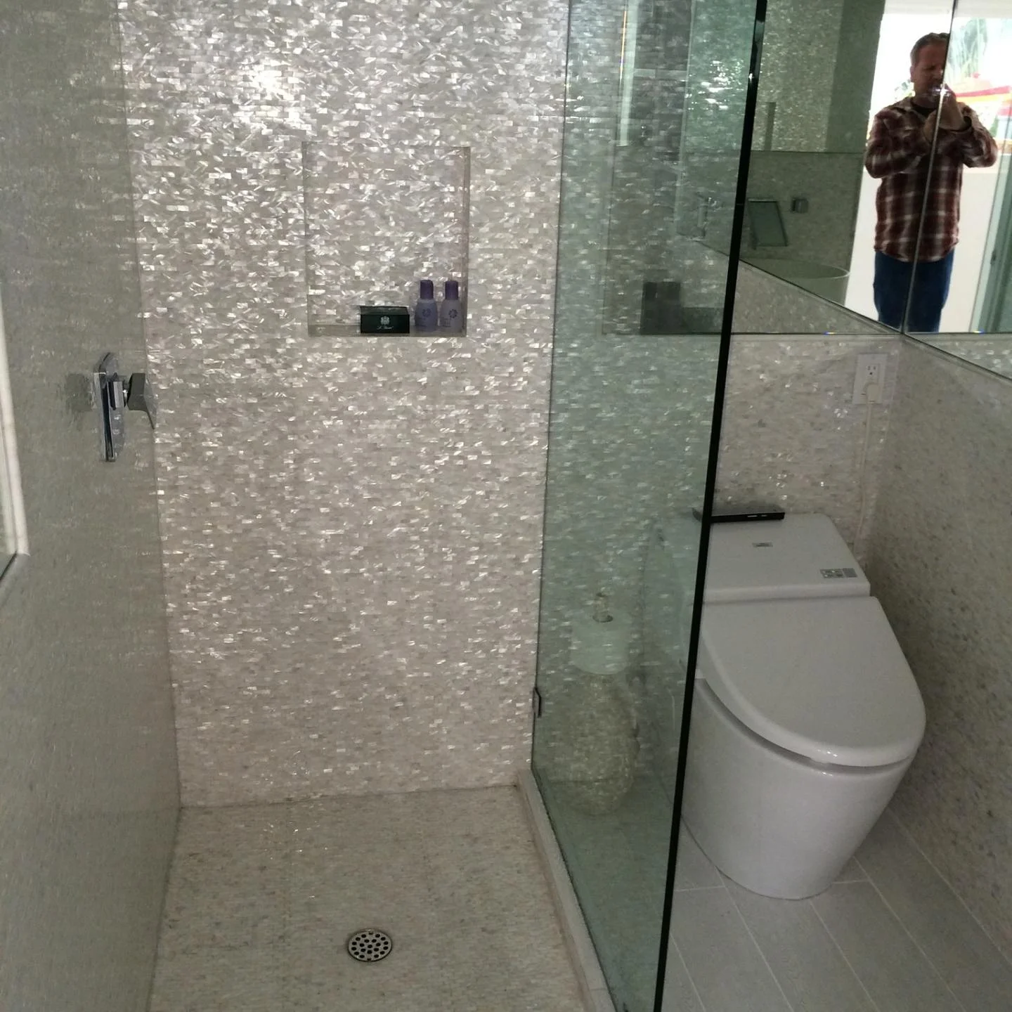 Frameless glass shower enclosure with iridescent tile walls and concrete floor in renovated bathroom
