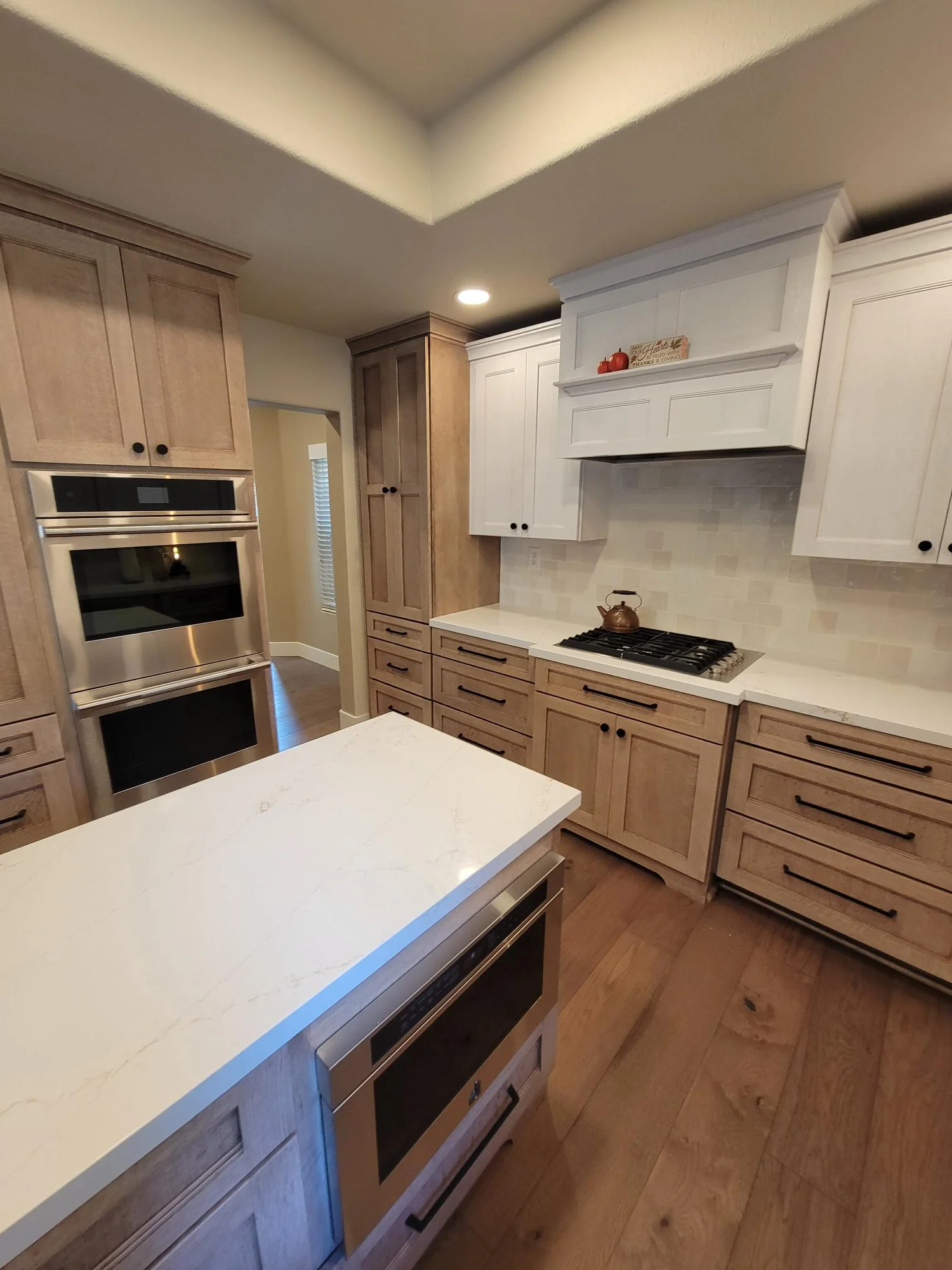 Kitchen with mixed wood and white cabinetry, quartz counters, stainless steel appliances, and hardwood floors