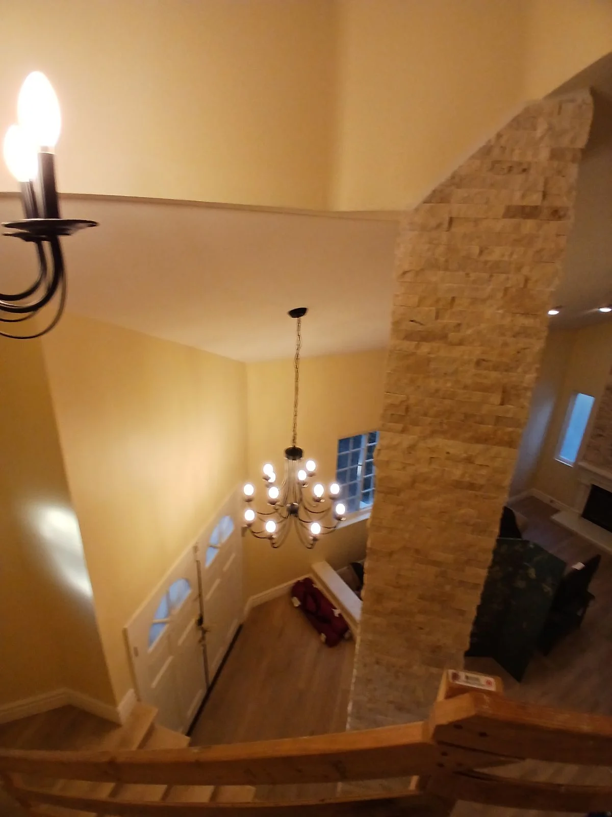 Stairwell with yellow painted walls, white wainscoting, stacked stone accent wall, and chandelier lighting