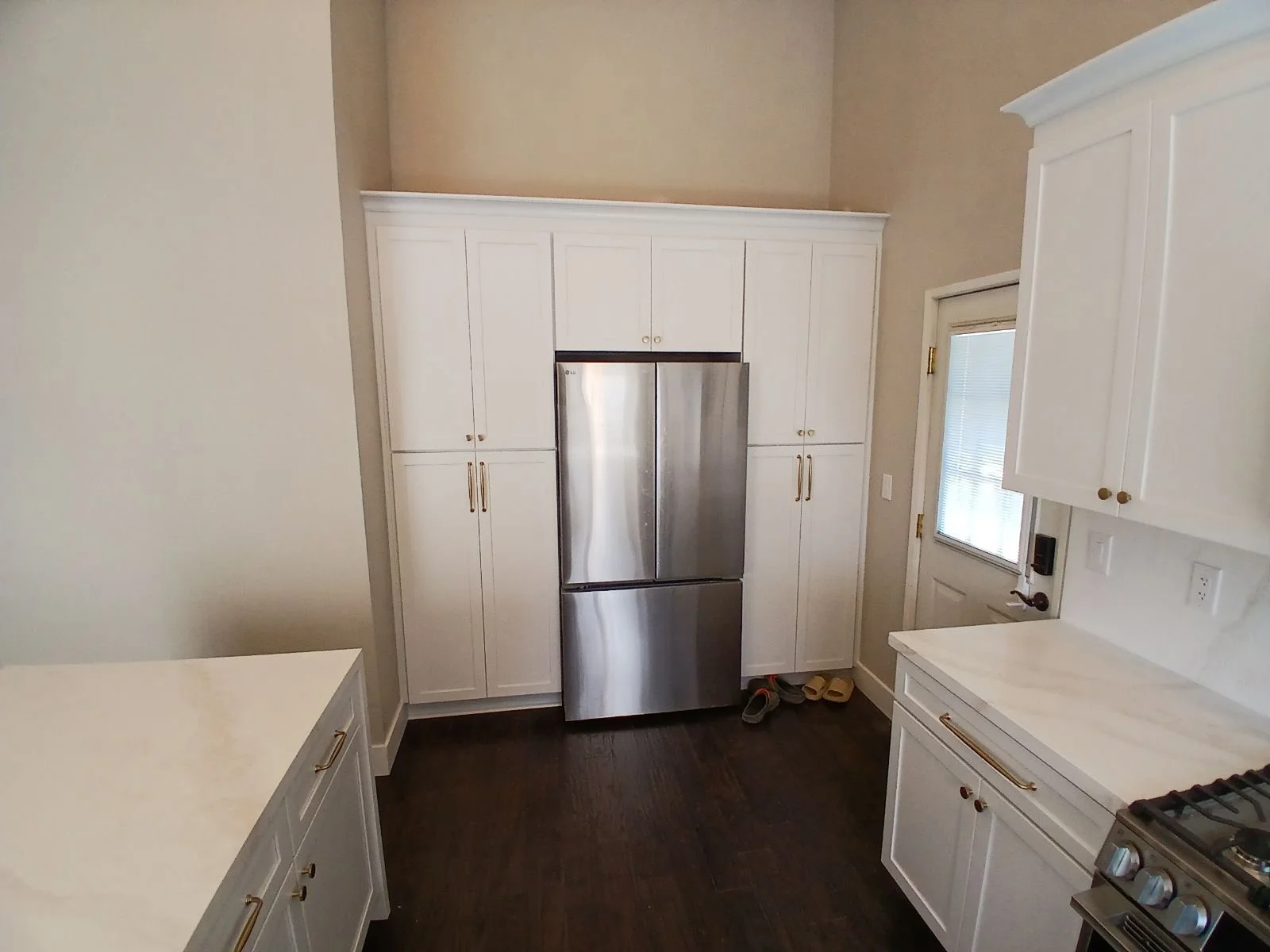 White kitchen cabinets with quartz counters, stainless steel refrigerator, and dark hardwood flooring
