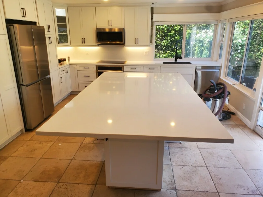 Modern kitchen with white cabinets, quartz island countertop, stainless steel appliances, and large windows