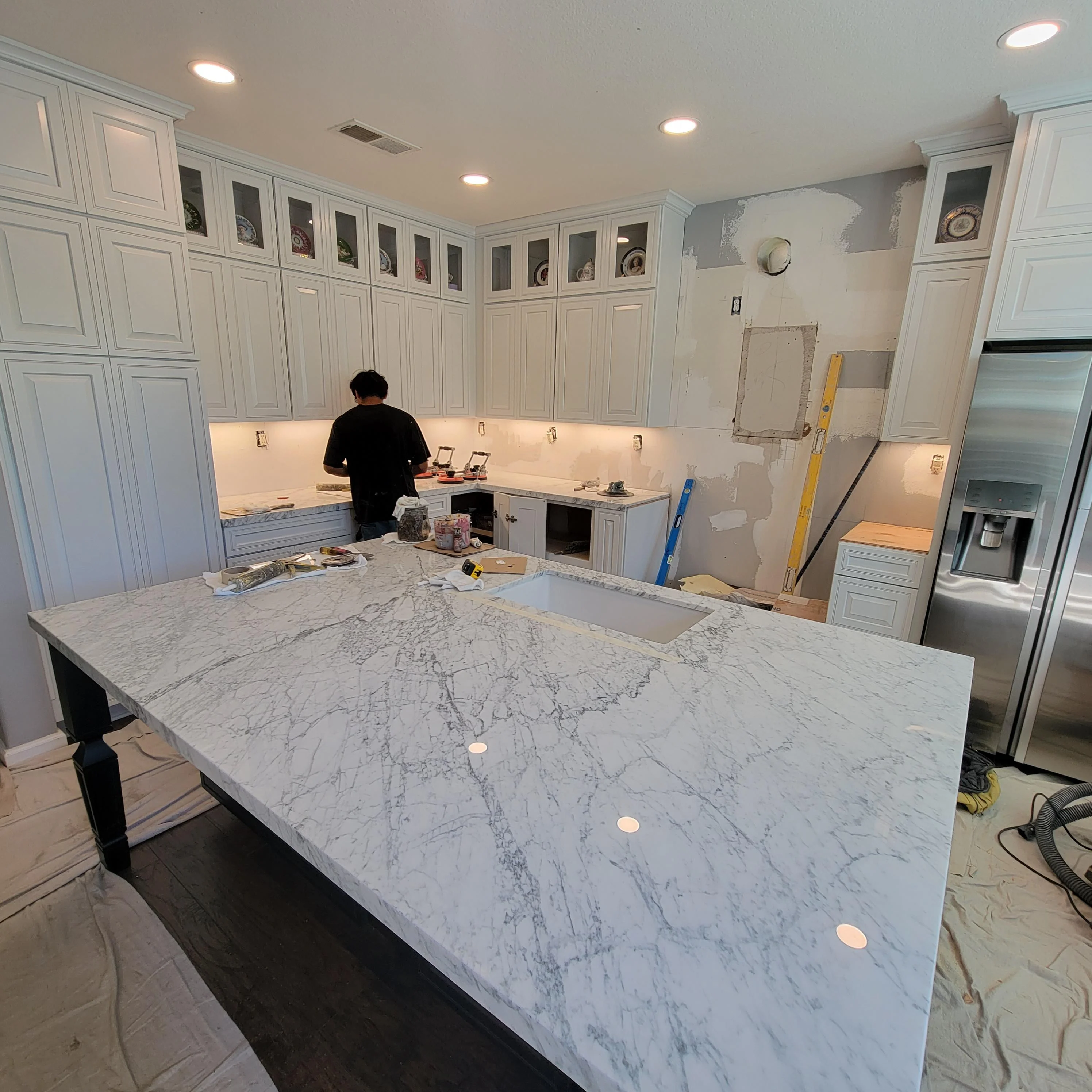 Kitchen renovation in progress with white cabinetry, marble island countertop, and stainless steel refrigerator