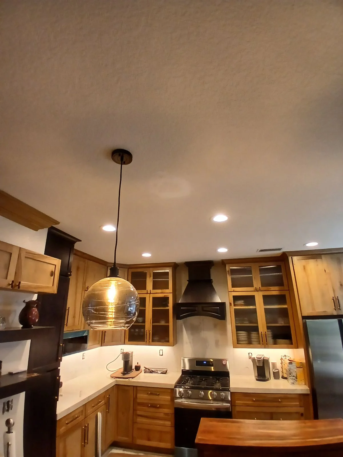 Kitchen with wood cabinetry, white counters, gas range, black hood, and pendant lighting