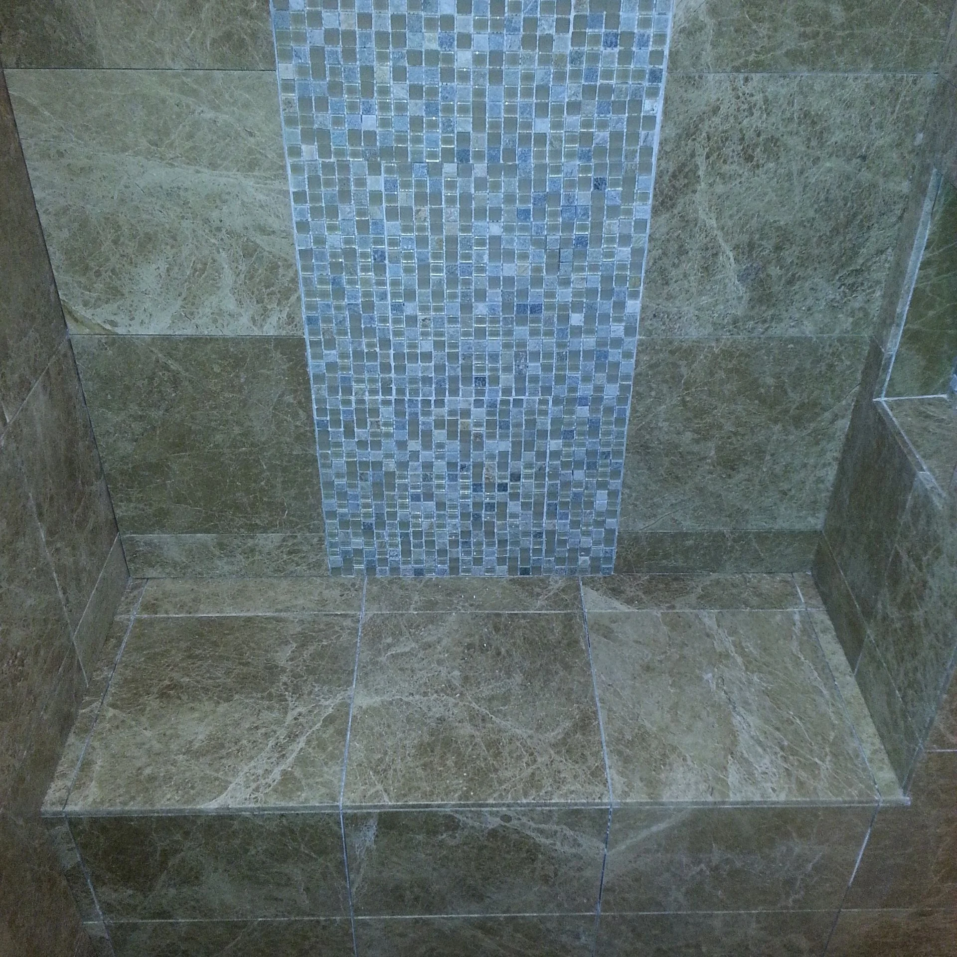 Shower interior with gray stone tile walls and blue glass mosaic tile accent panel