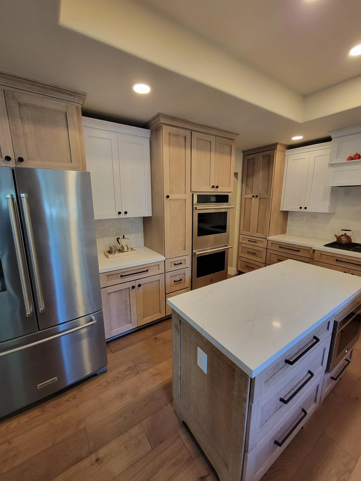 Kitchen with mixed wood and white cabinetry, white quartz island, stainless steel appliances, hardwood floors