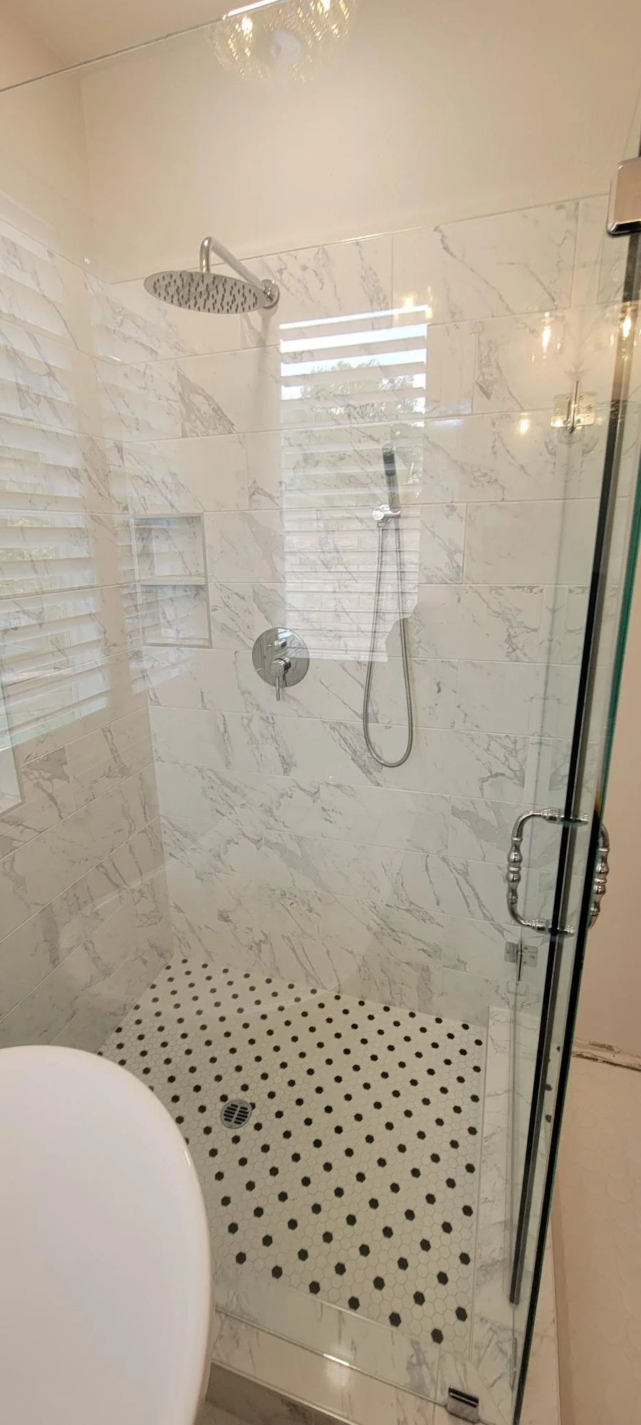 Marble tile shower with frameless glass door, rainfall showerhead, and mosaic floor
