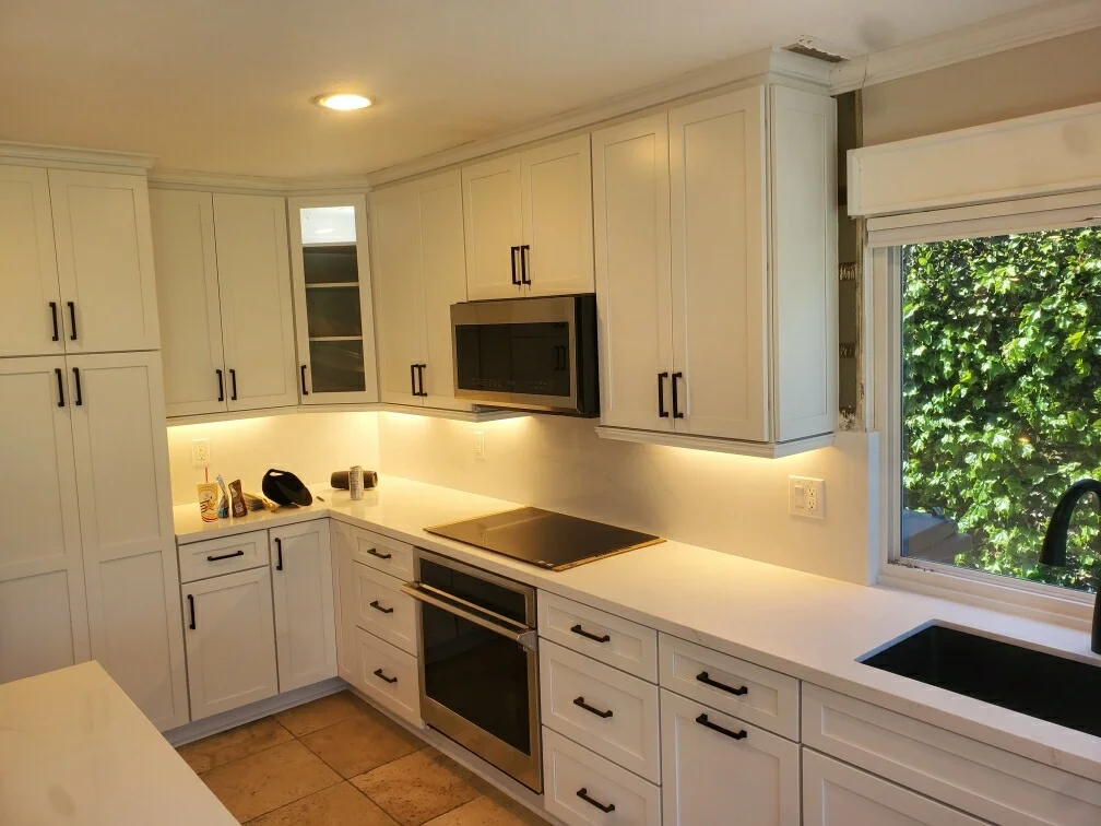 White kitchen cabinetry with quartz counters, stainless steel appliances, and under-cabinet lighting