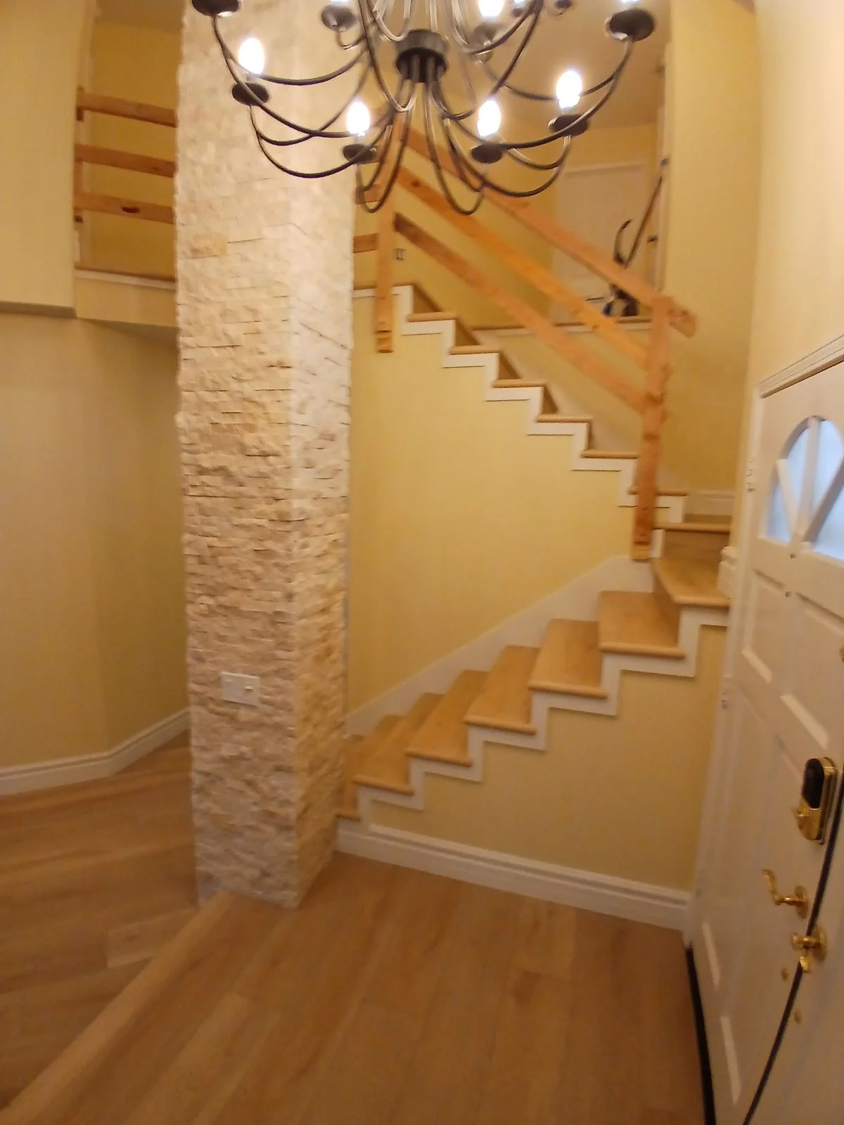 Wooden staircase with white risers, white brick column, yellow walls, and chandelier lighting