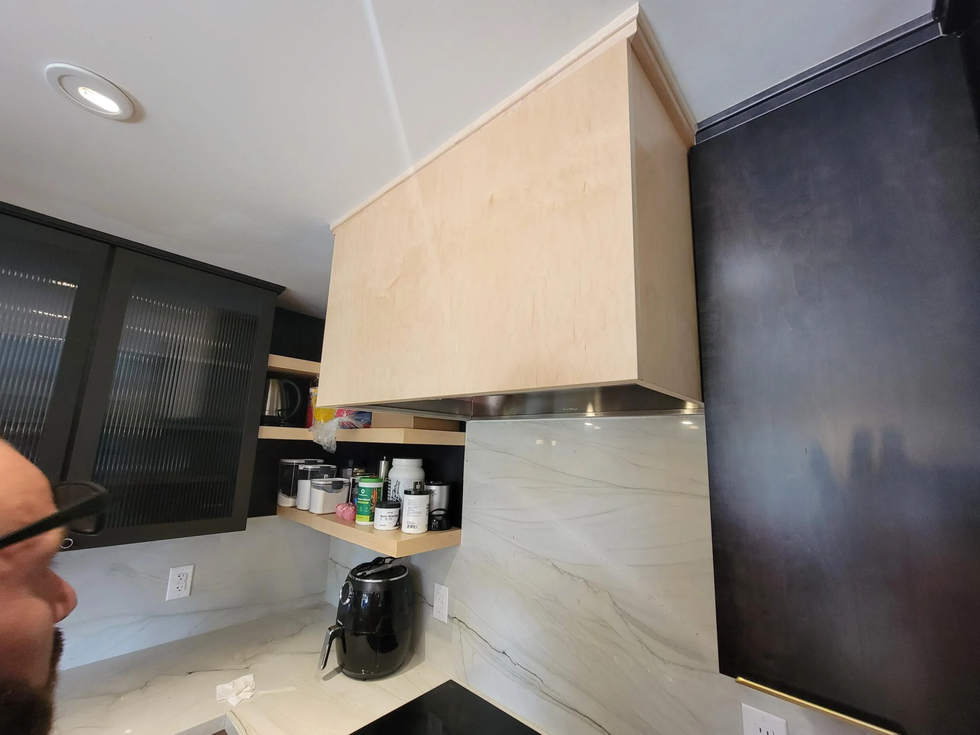 Kitchen with light wood and black cabinetry, marble tile backsplash, stainless hood, and recessed lighting