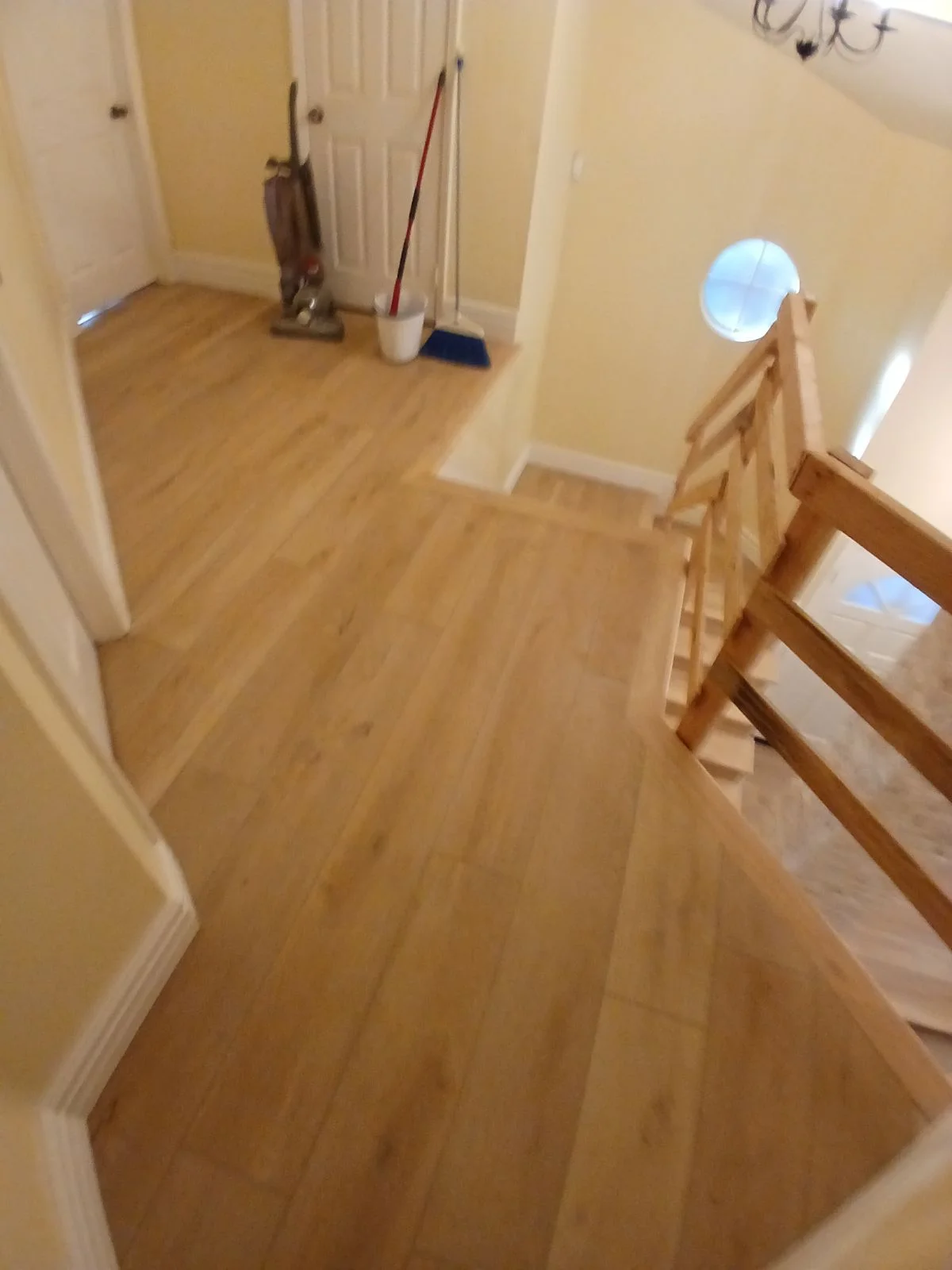 Laminate wood-grain flooring installed in hallway with white trim and wooden stair railing