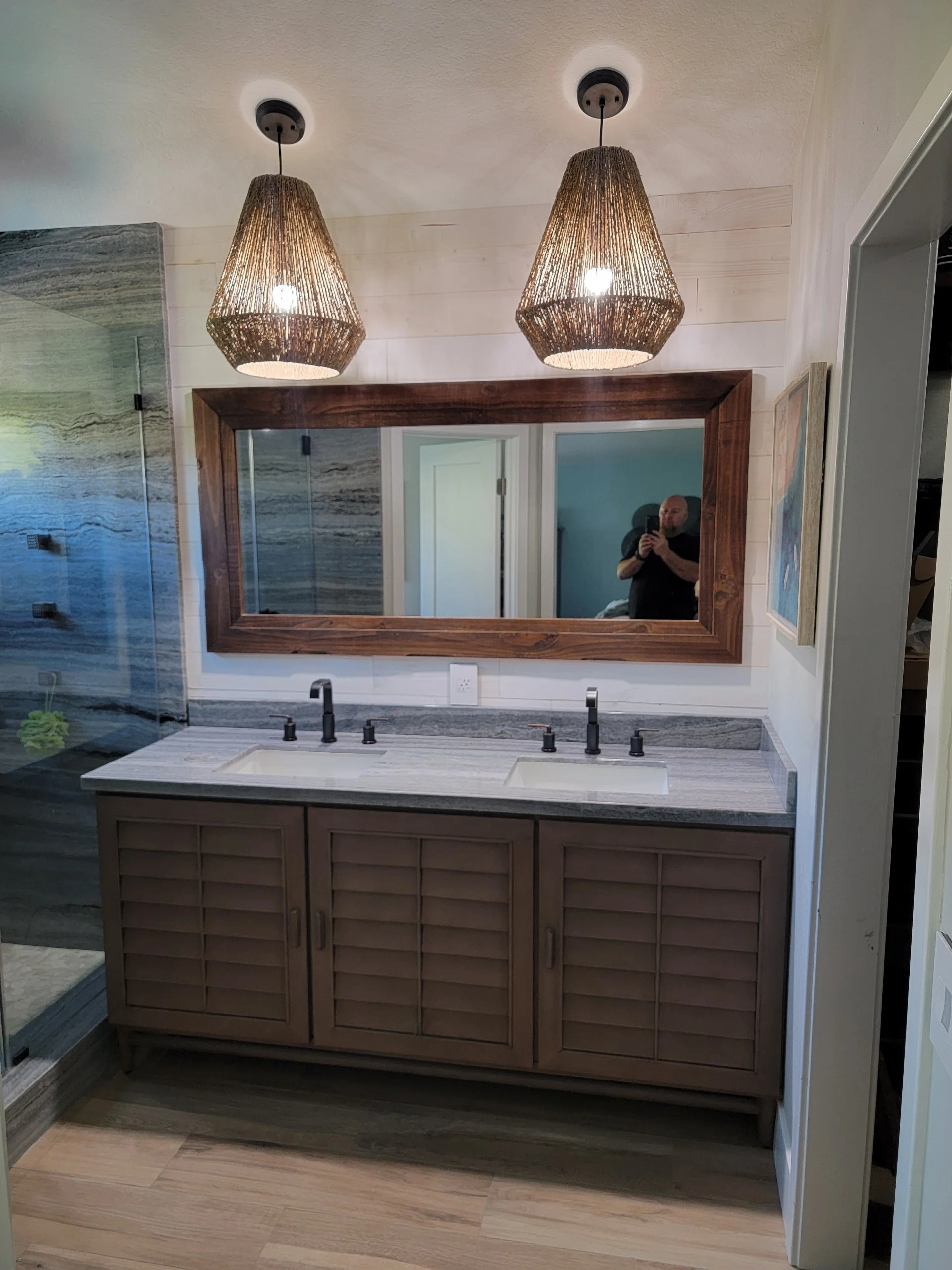 Master bathroom with dark wood vanity, gray stone countertop, woven pendant lights, and framed mirror