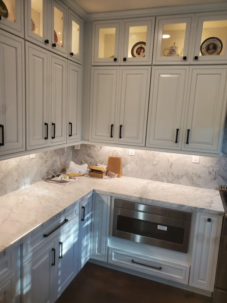 Light gray kitchen cabinets with glass doors, marble countertops and backsplash, stainless steel microwave