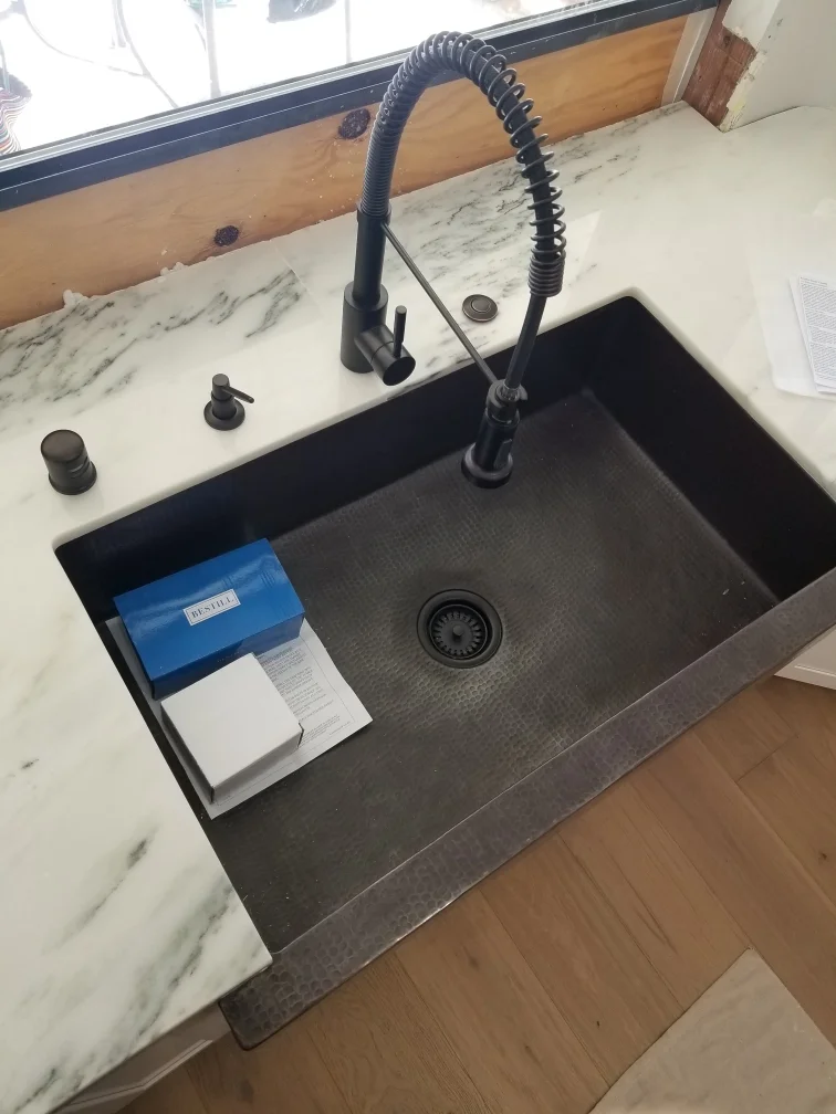 Black composite undermount sink with pull-down faucet, marble countertop, and wood cabinetry