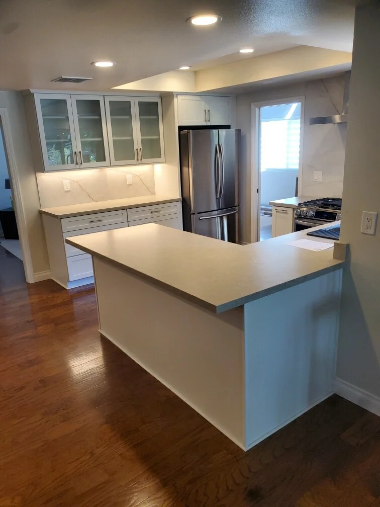 White kitchen with quartz island, glass cabinets, stainless steel appliances, and recessed lighting