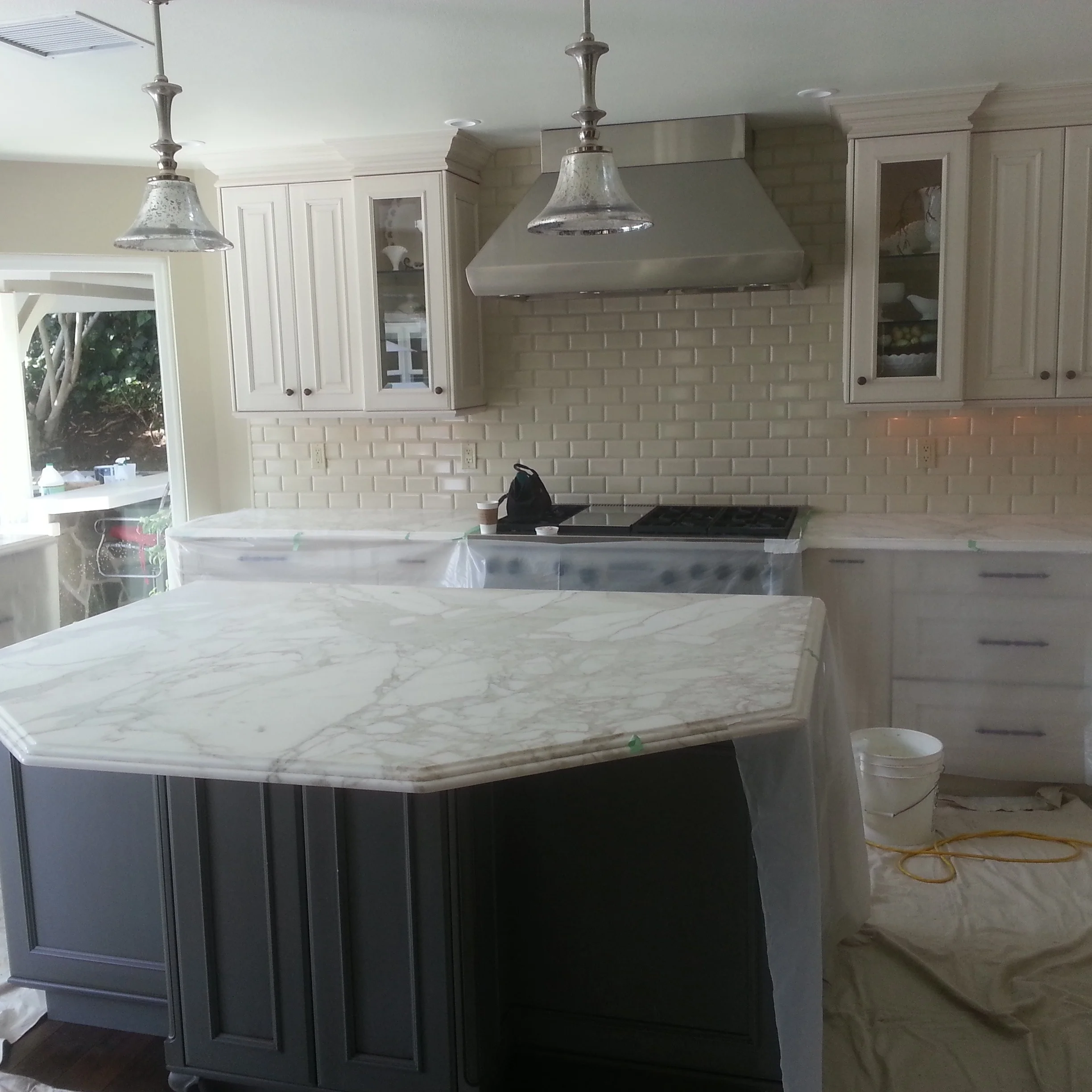 Kitchen with white cabinets, marble island, subway tile backsplash, and stainless steel hood